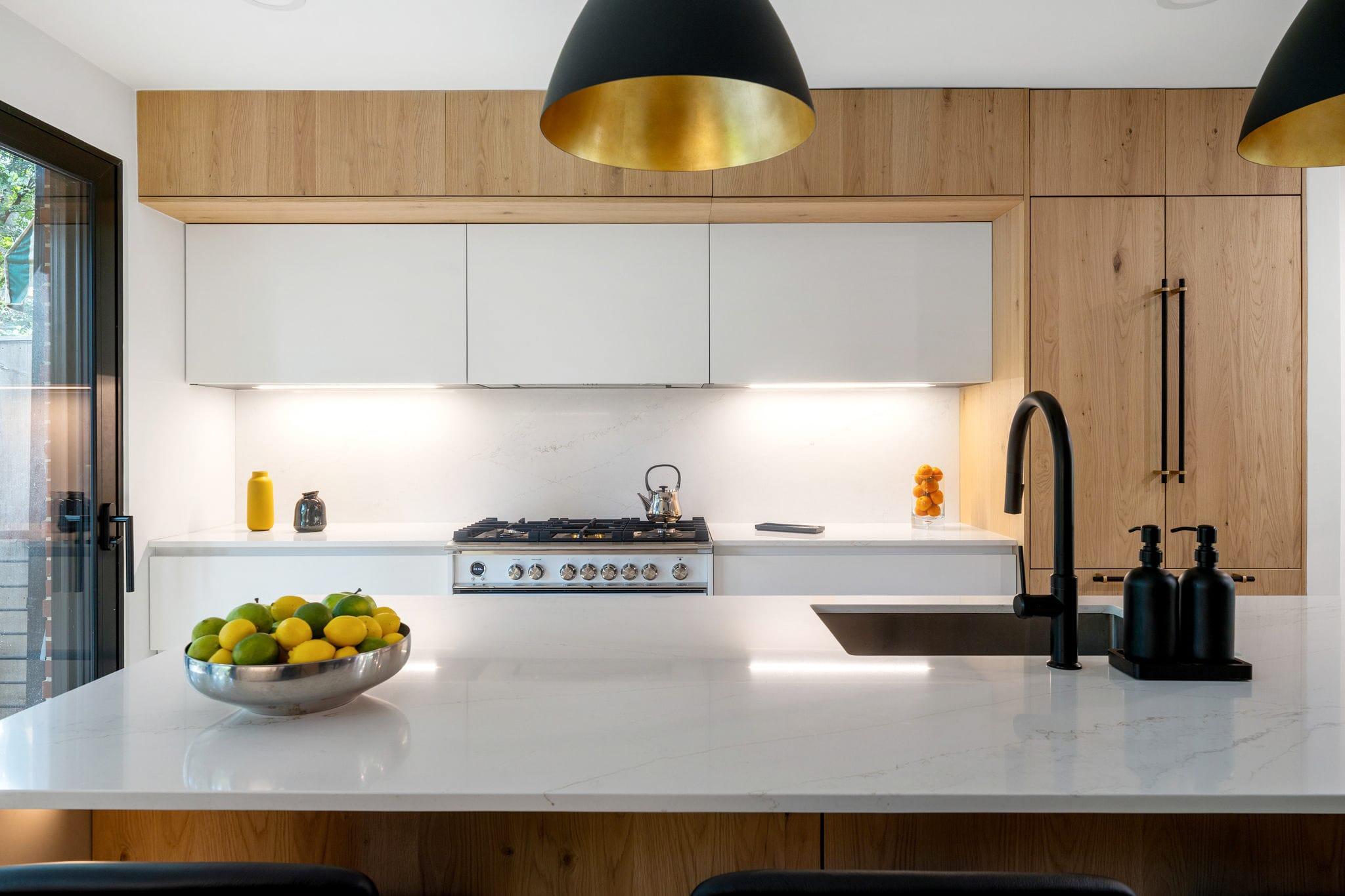 Kitchen with a white island under black pendants, oak tall units behind