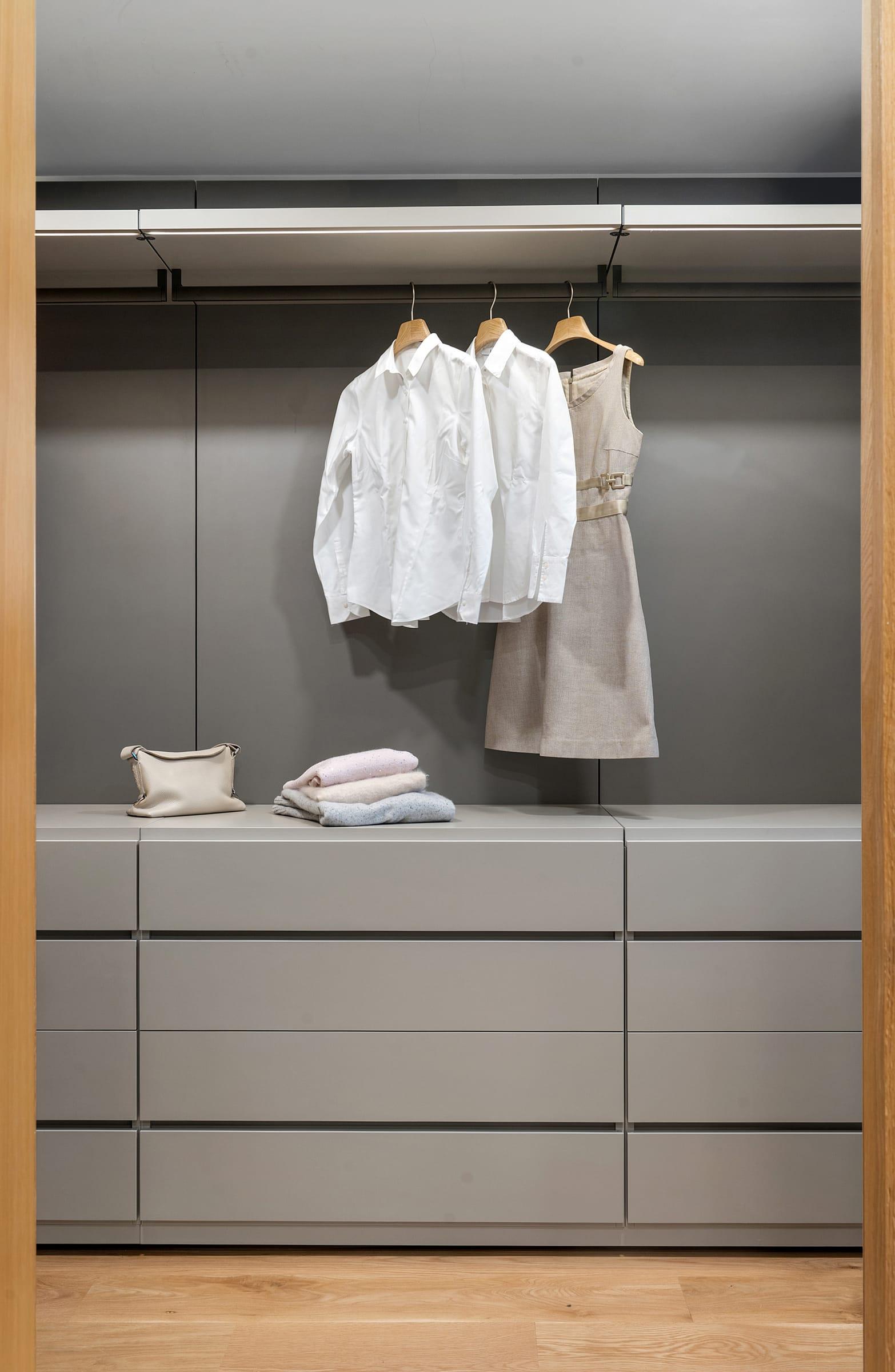Grey walk-in wardrobe with hanging shirts over drawers