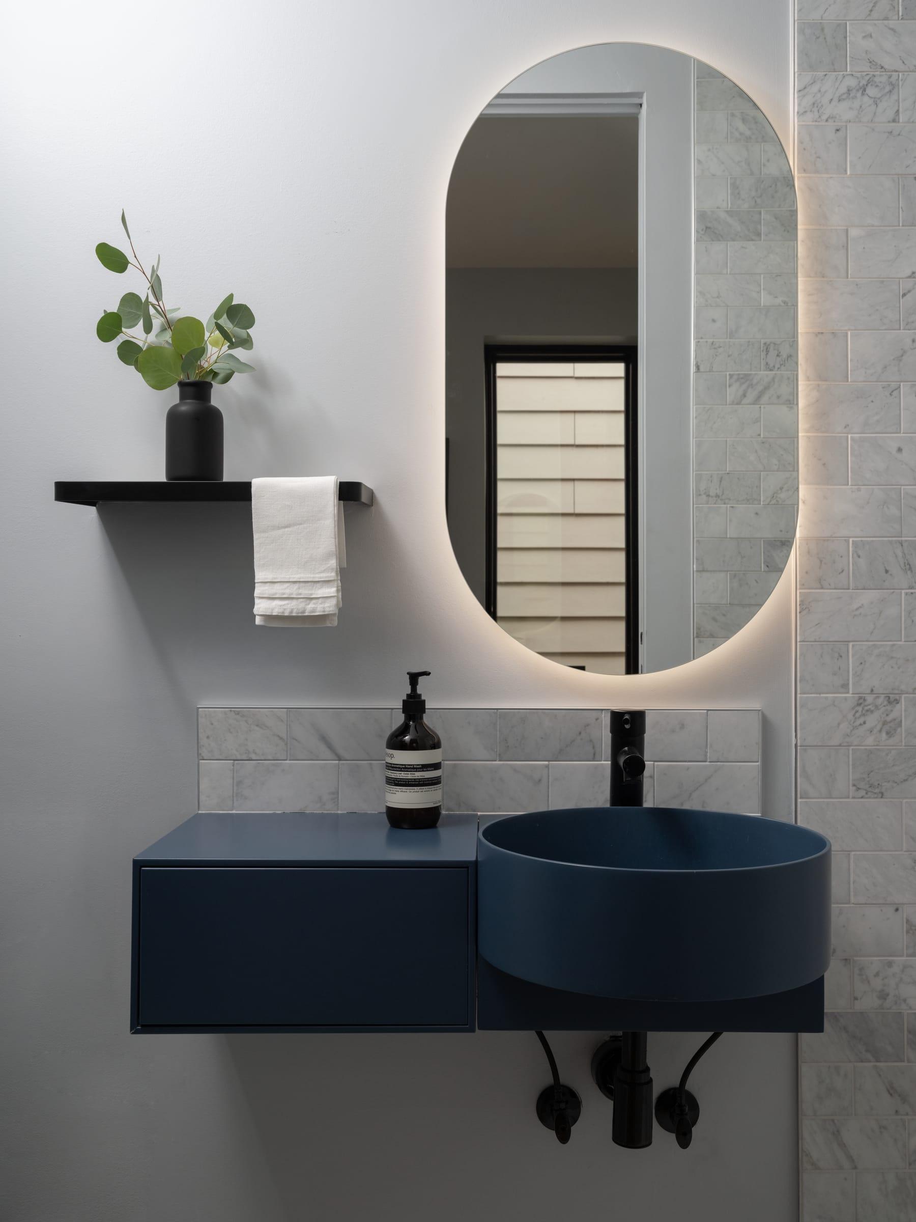 Navy wall-hung basin under an oval lit mirror