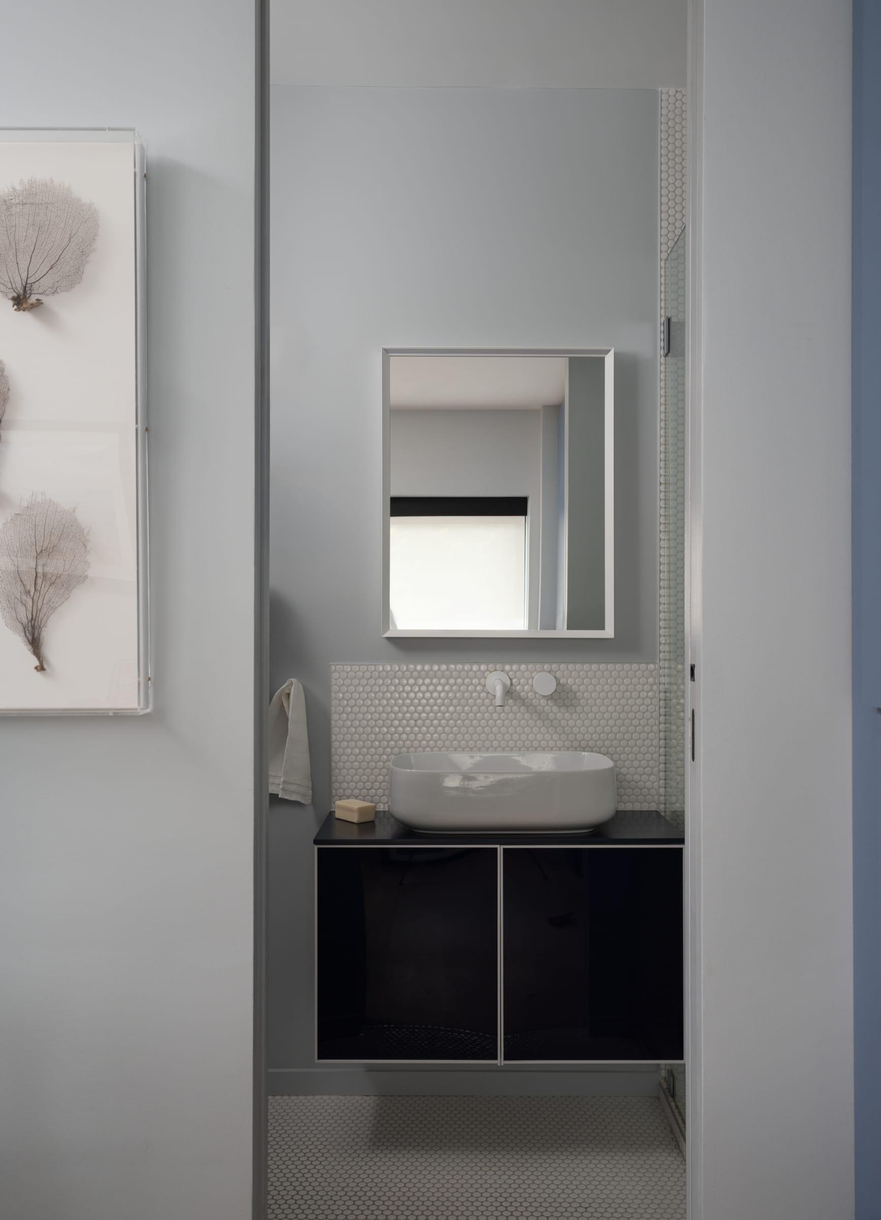 Black vanity under a mirror cabinet in a narrow bathroom