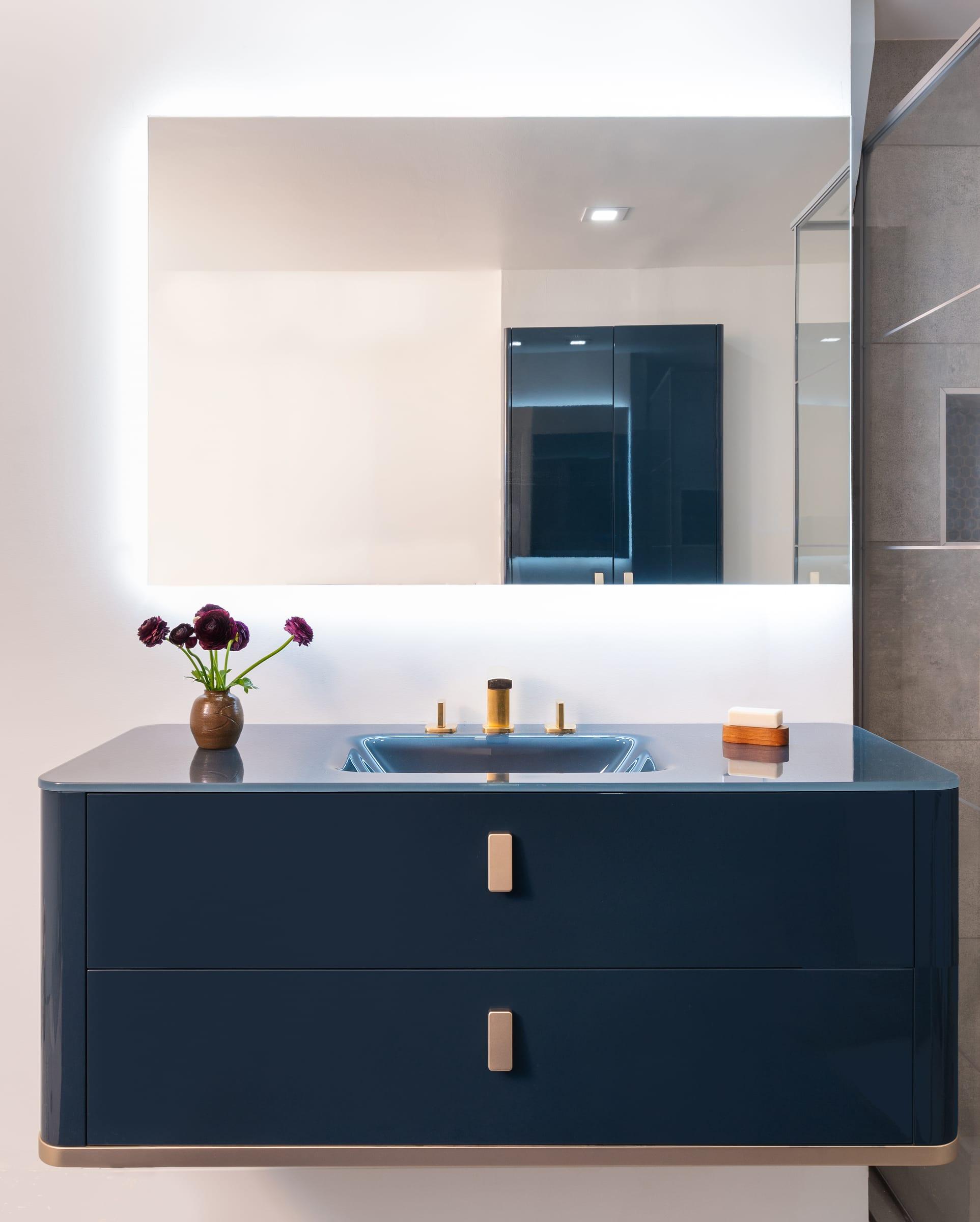 Navy vanity with brass handles under a lit mirror