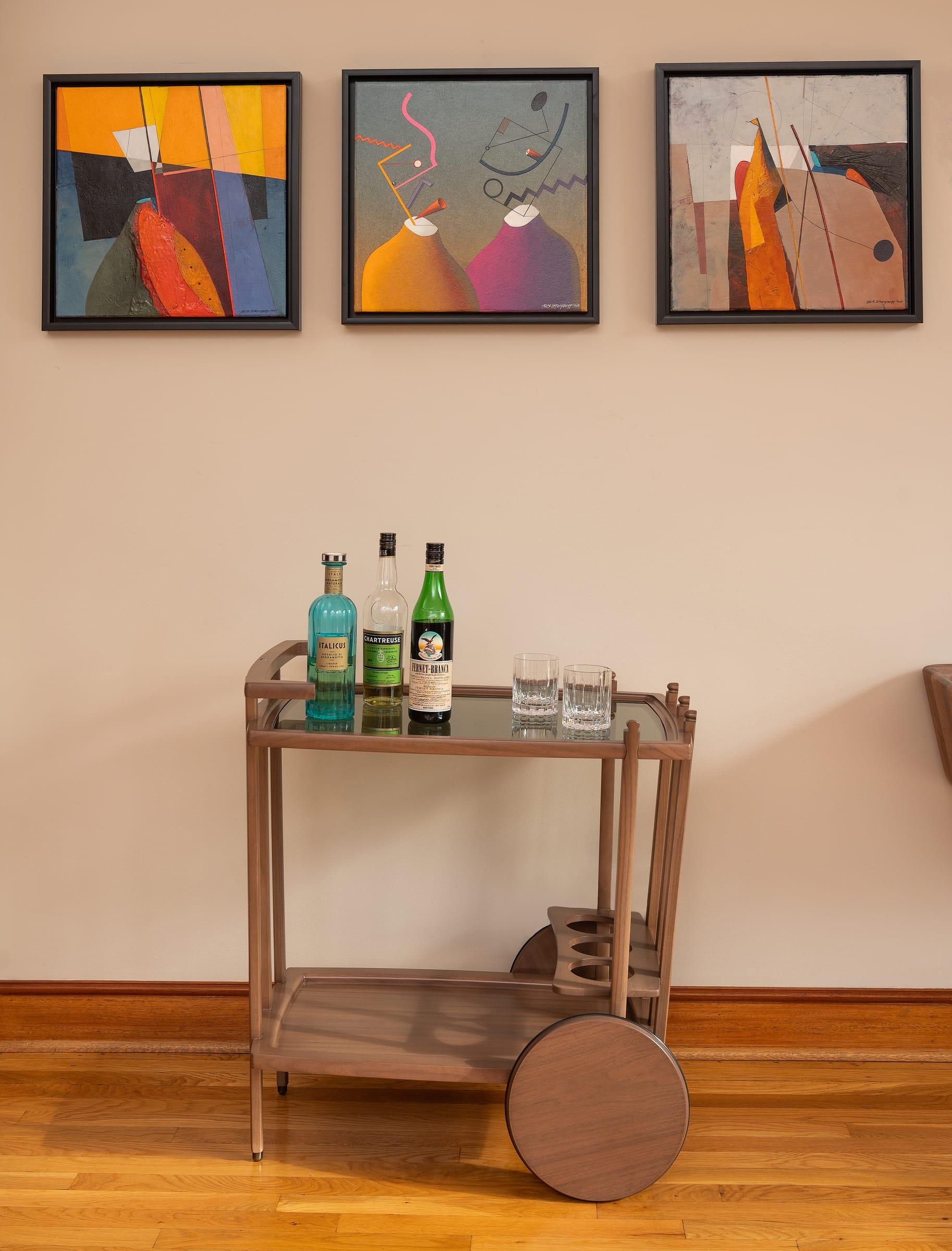 Walnut bar cart under three paintings