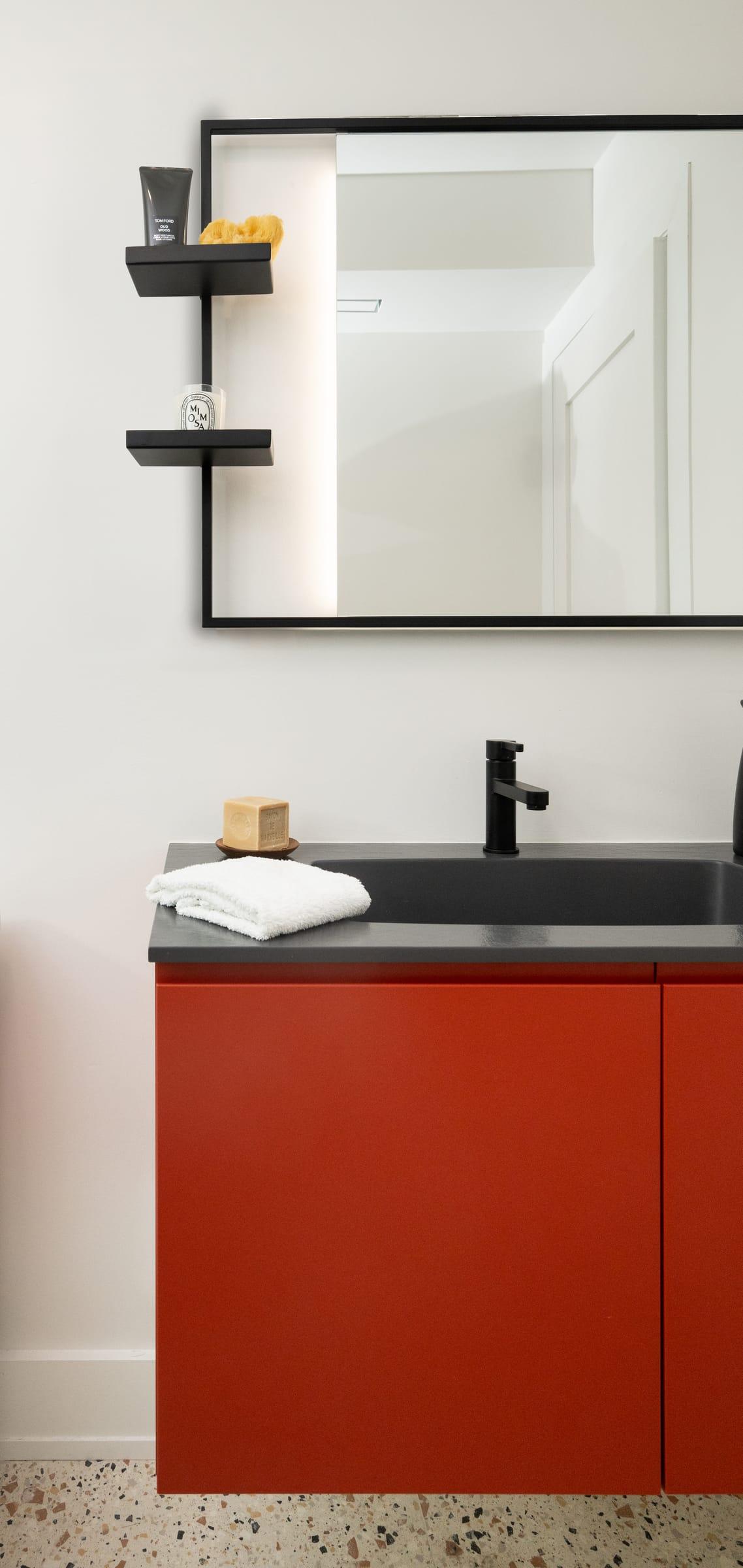 Red vanity with a black top under a mirror and shelf