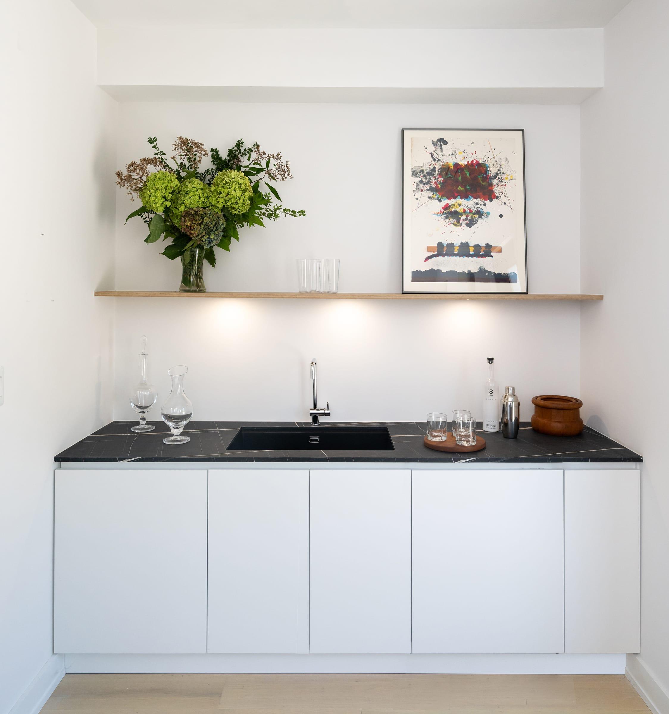 White cabinets with a black worktop under a shelf of flowers