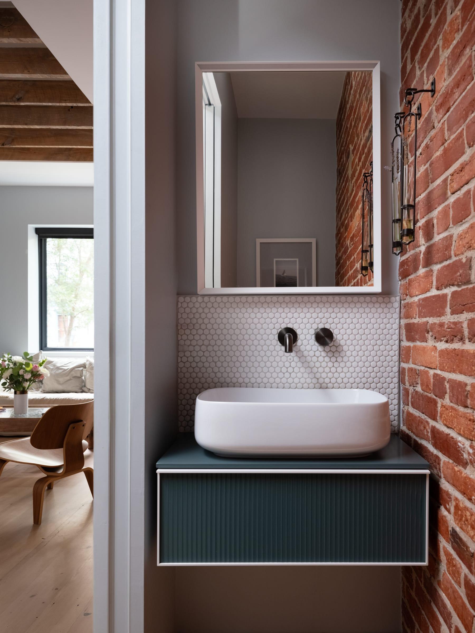 White basin on a dark green vanity against a brick wall