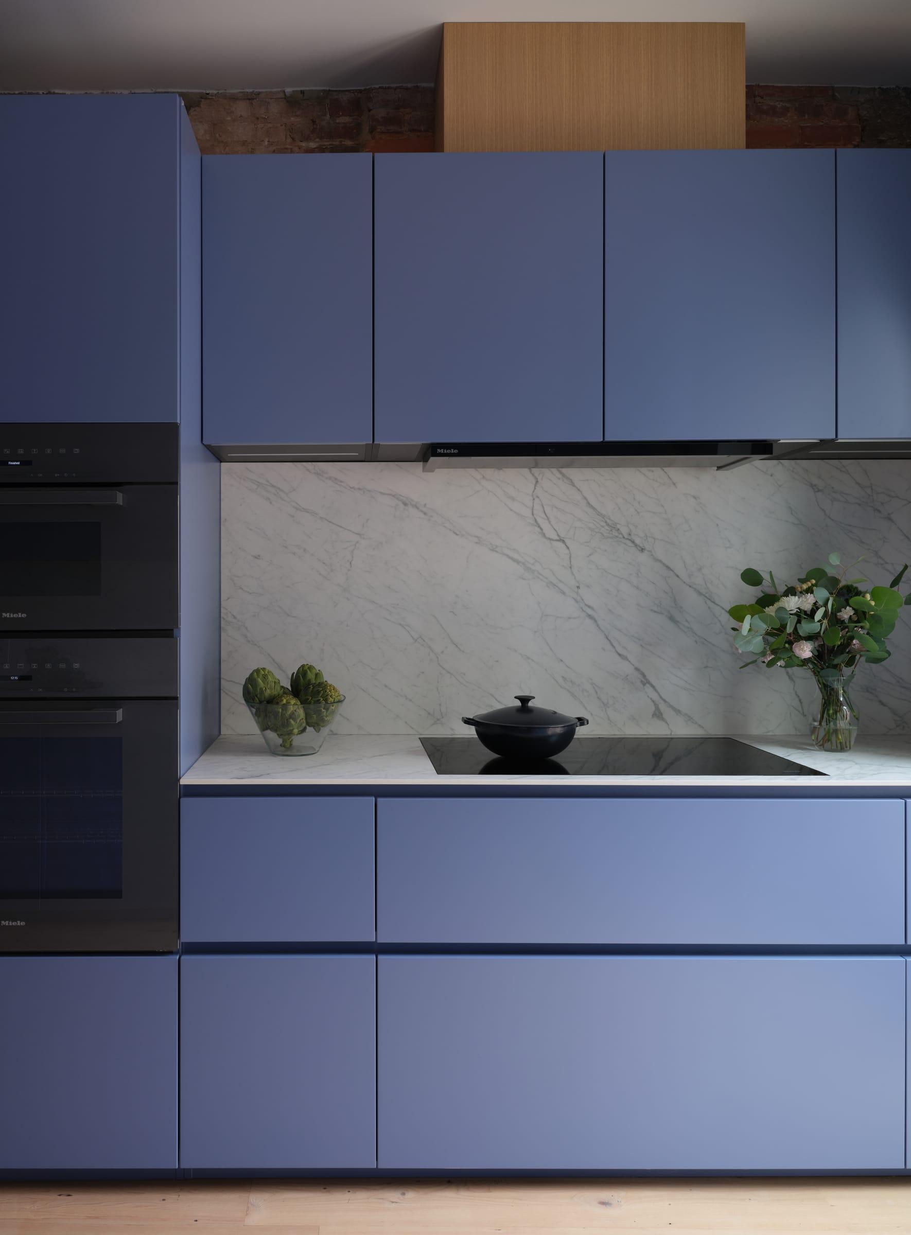 Blue cabinets around a black hob and a marble splashback