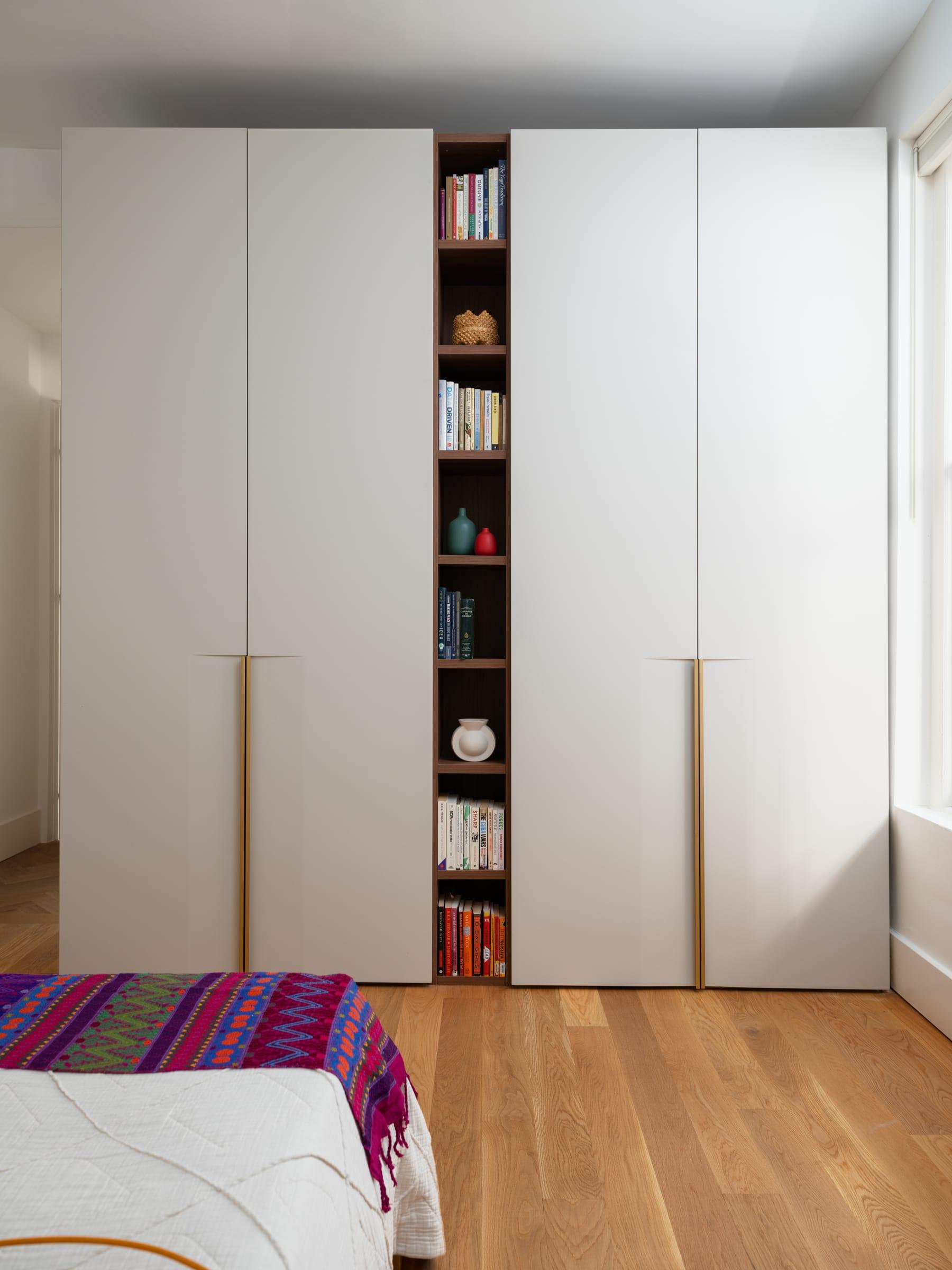 White wardrobe with a tall open bookcase beside a bed