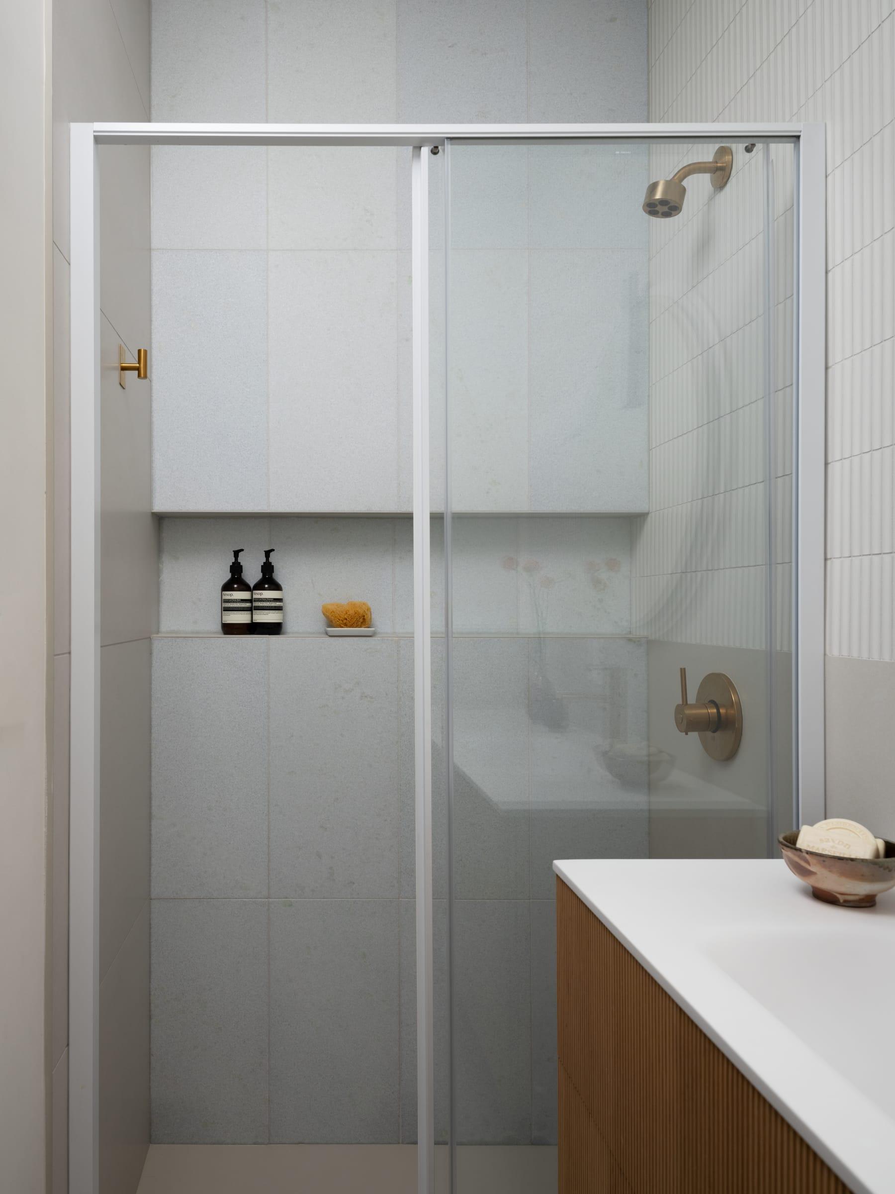Glass shower beside a walnut vanity with a white top