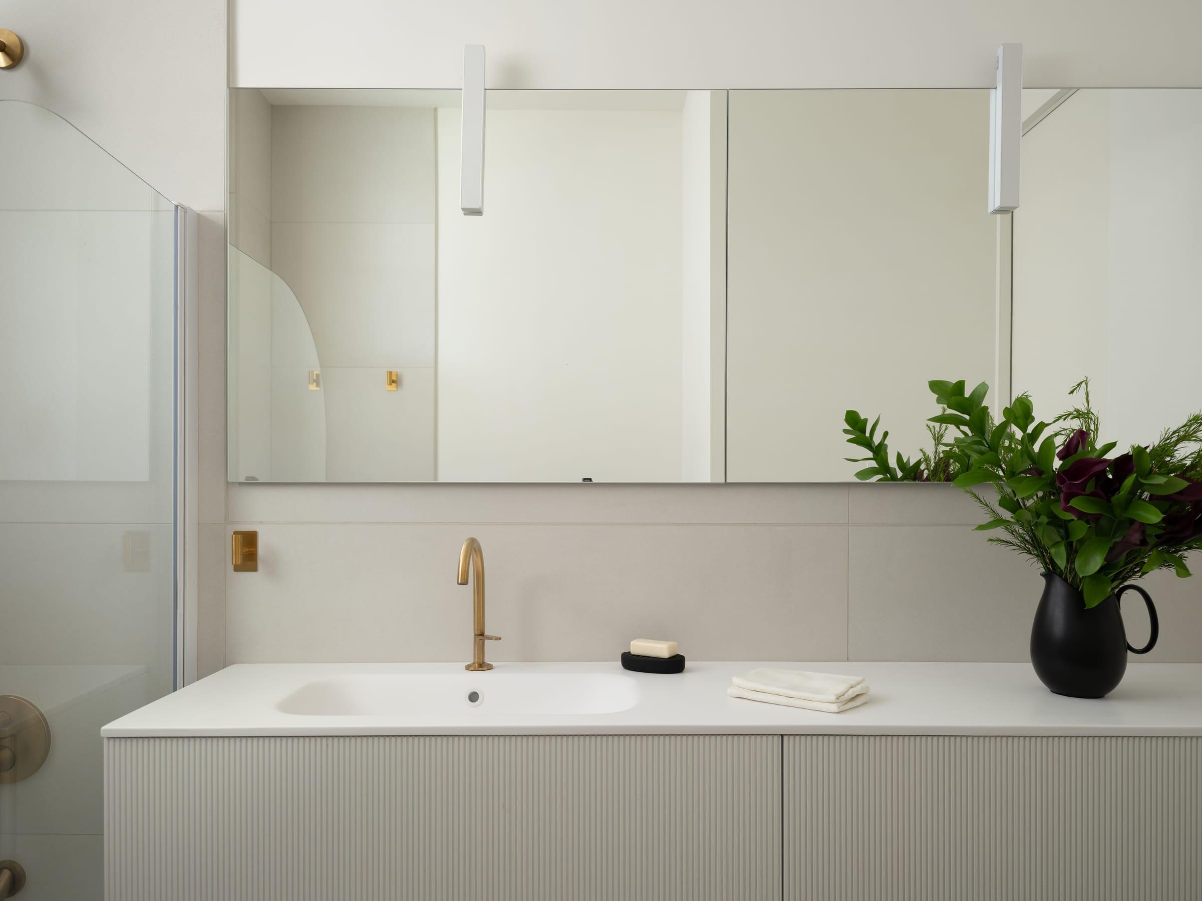 Long white vanity under a wide mirror with brass taps