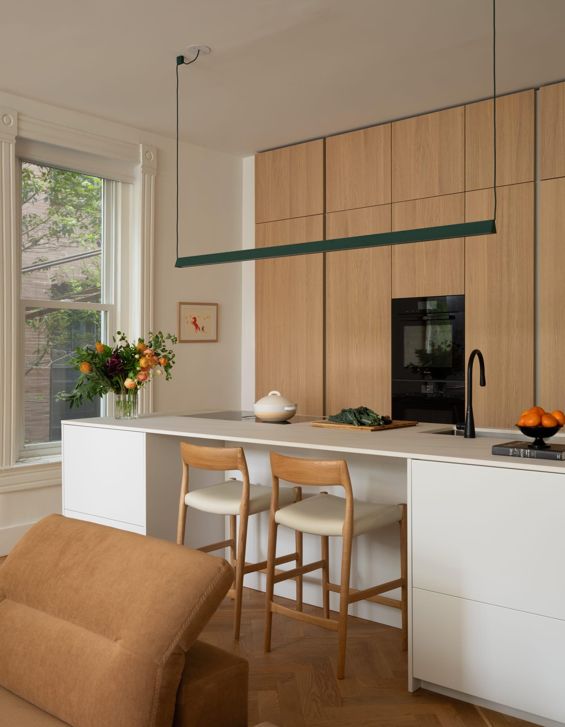 White island with stools before oak tall units and a black oven