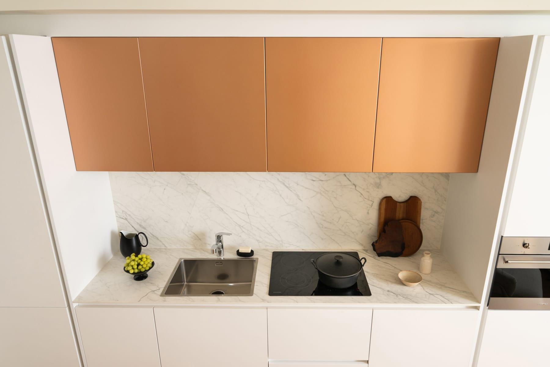 Copper wall cabinets over a white worktop with a hob and sink