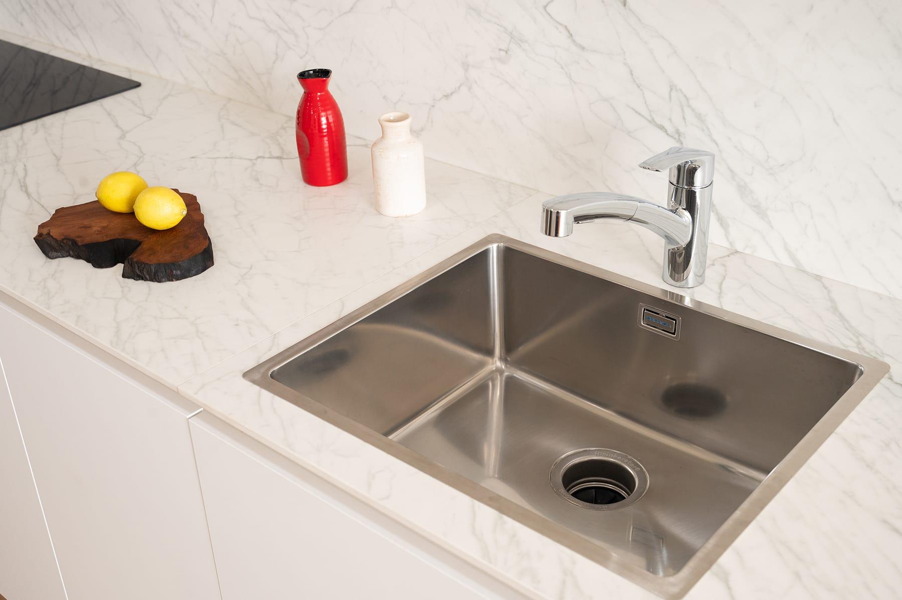 Steel sink in a white marble worktop with a bottle and lemons