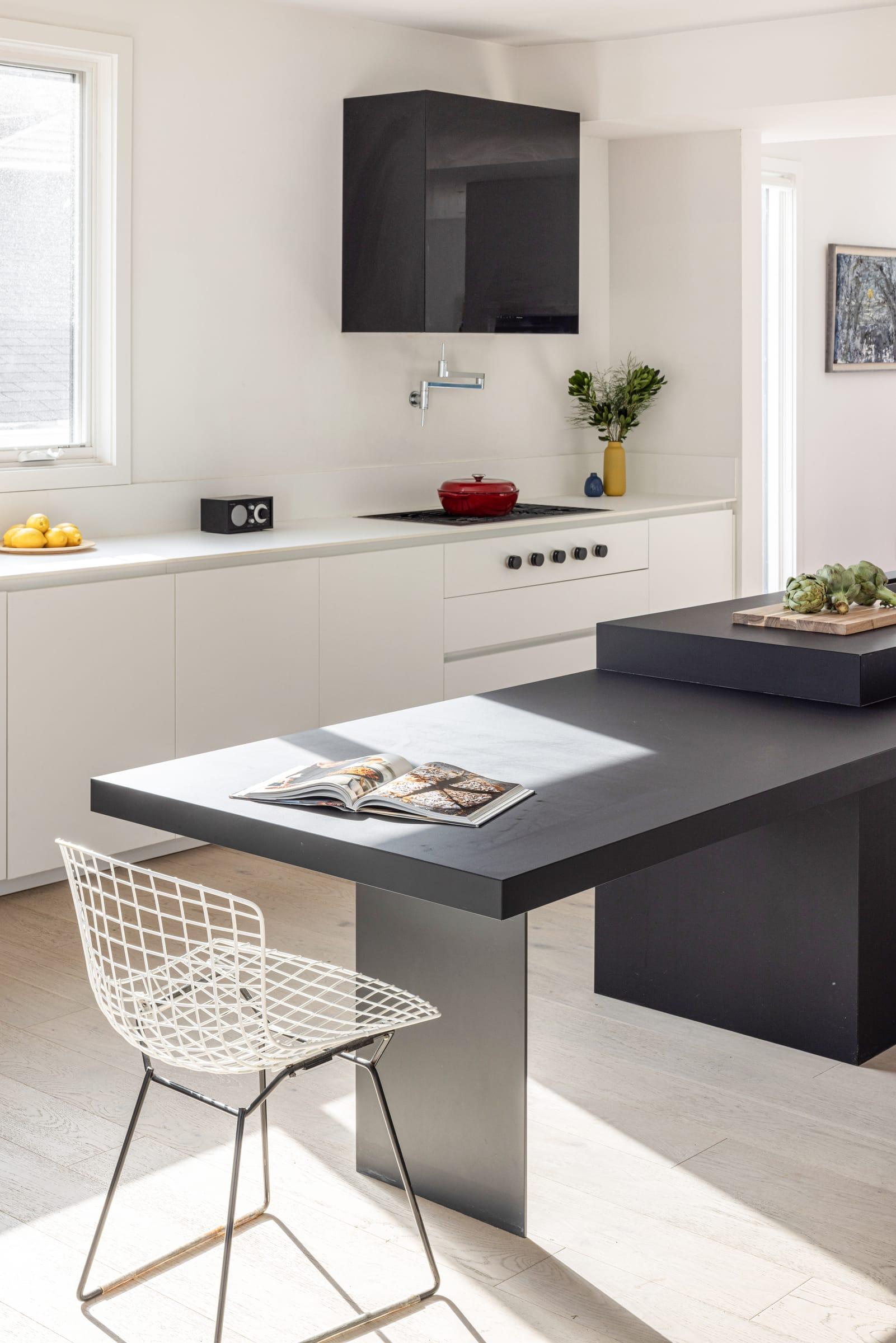 Dark grey island with a wire chair, white tall units behind