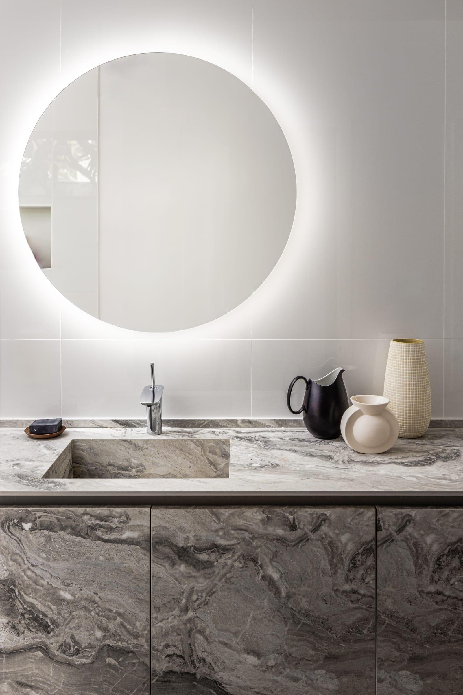Marble-faced vanity under a round lit mirror