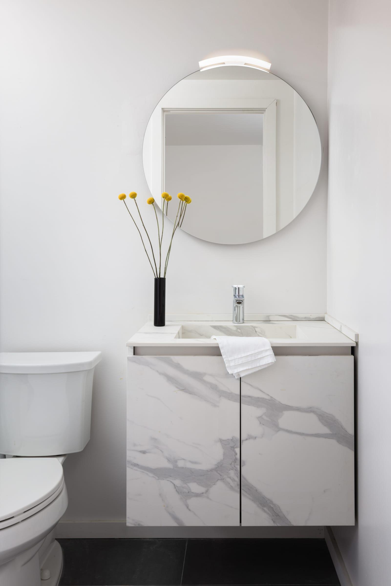Marble-faced vanity under a round mirror with a vase