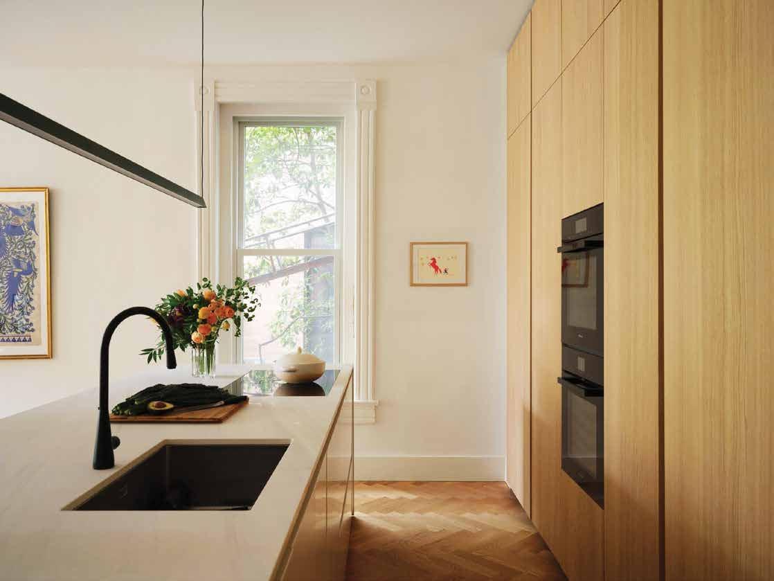 Kitchen in pale oak with a black tap and tall ovens, a painting by the window