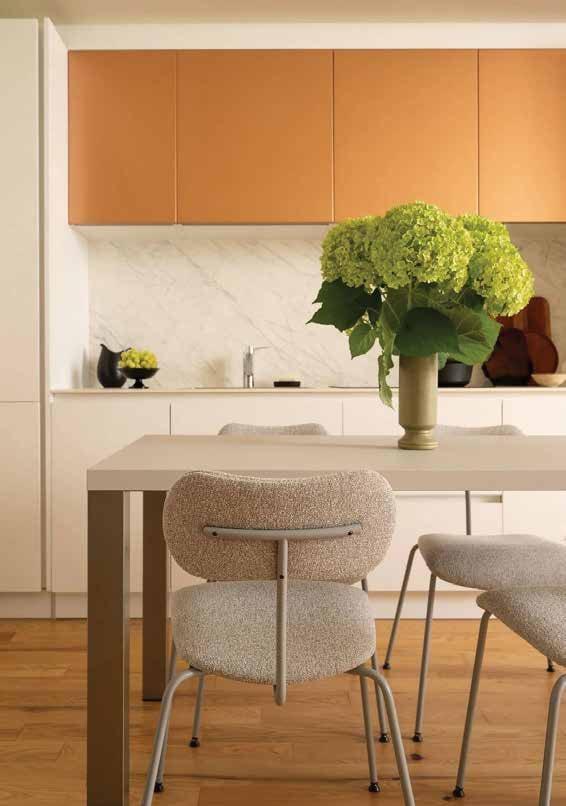 Dining table with upholstered chairs under copper wall cabinets and a vase of hydrangeas