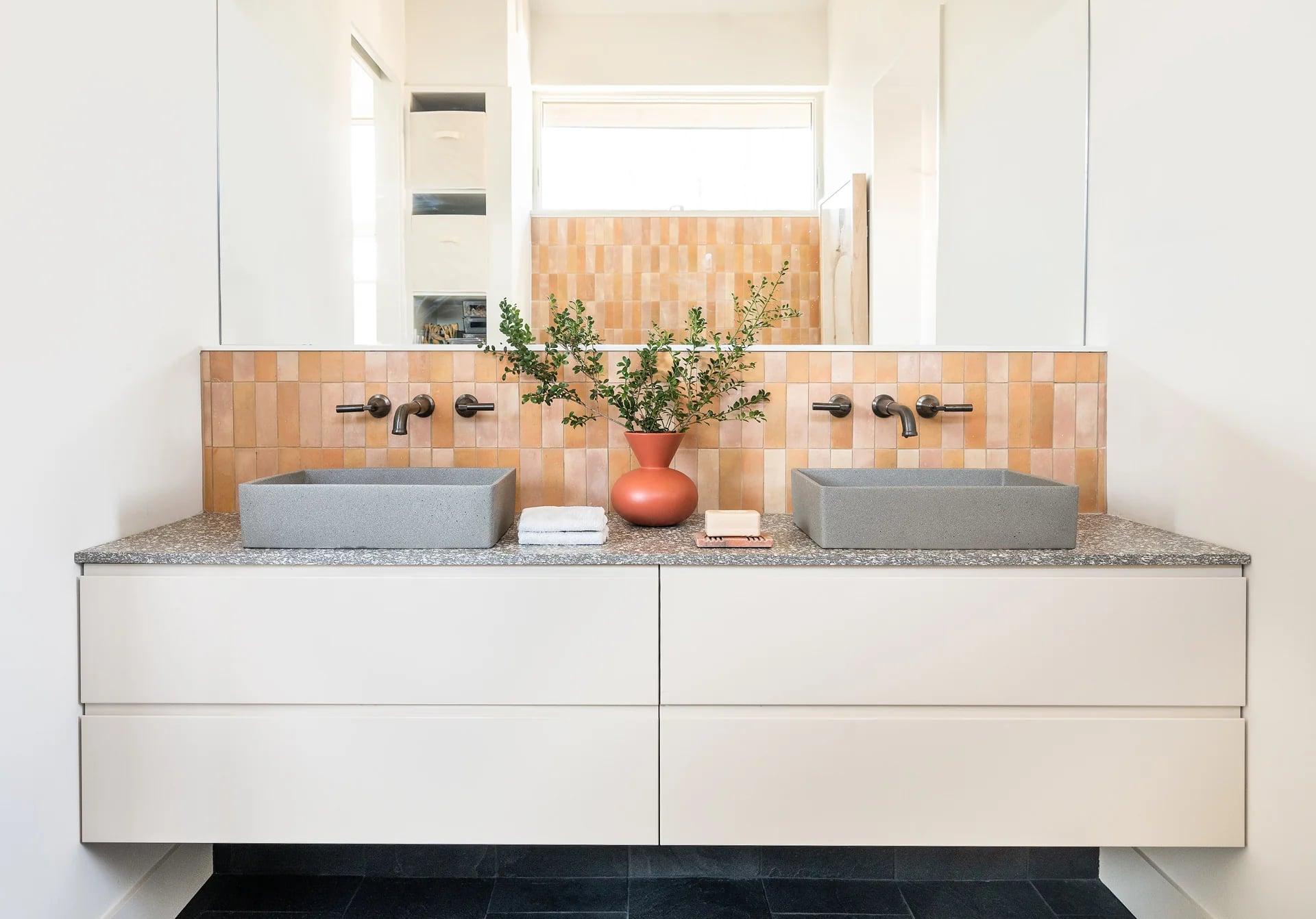 White basin on a matt lacquered vanity with a black soap dispenser and a plant