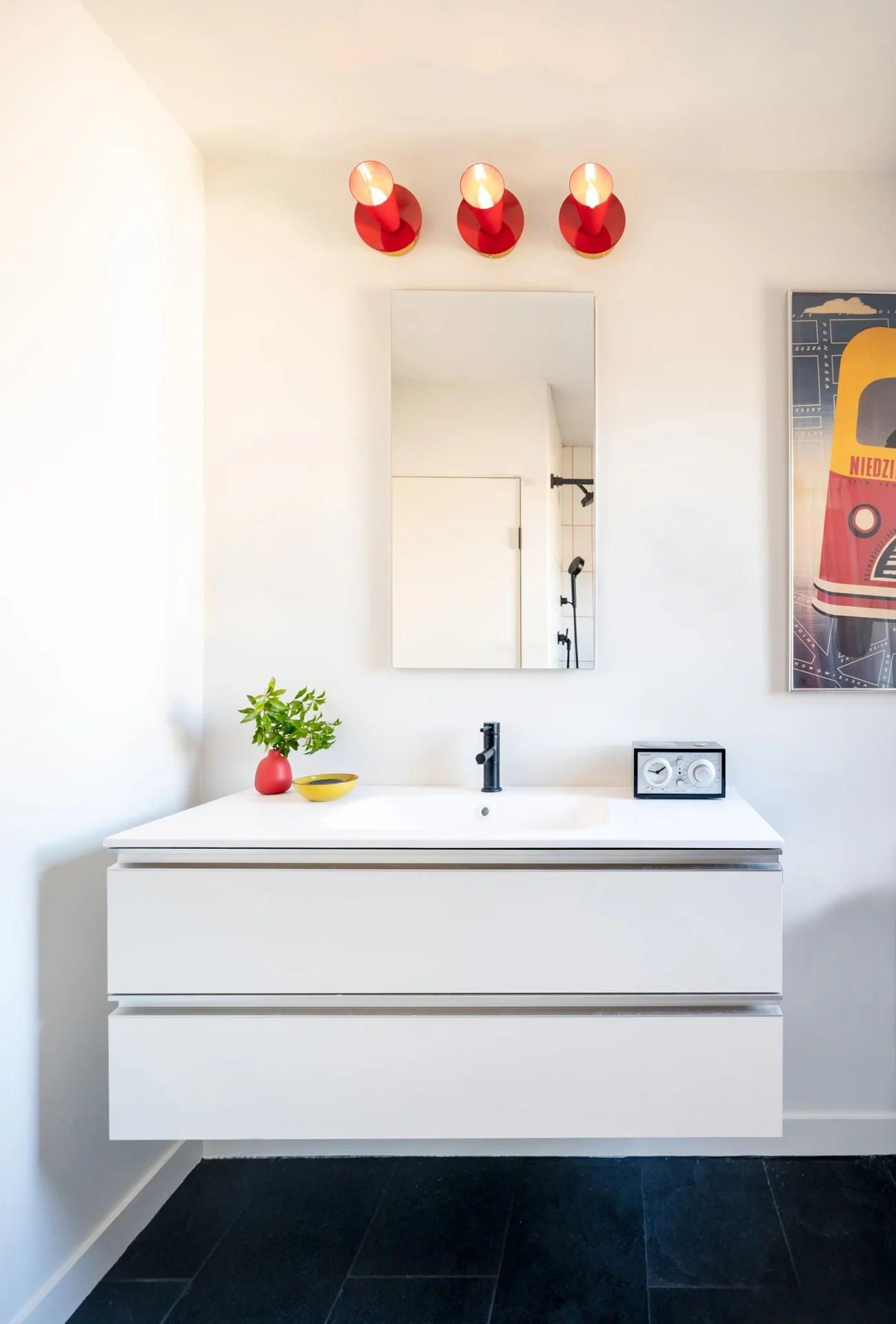 White vanity under a mirror with three red pendant lights