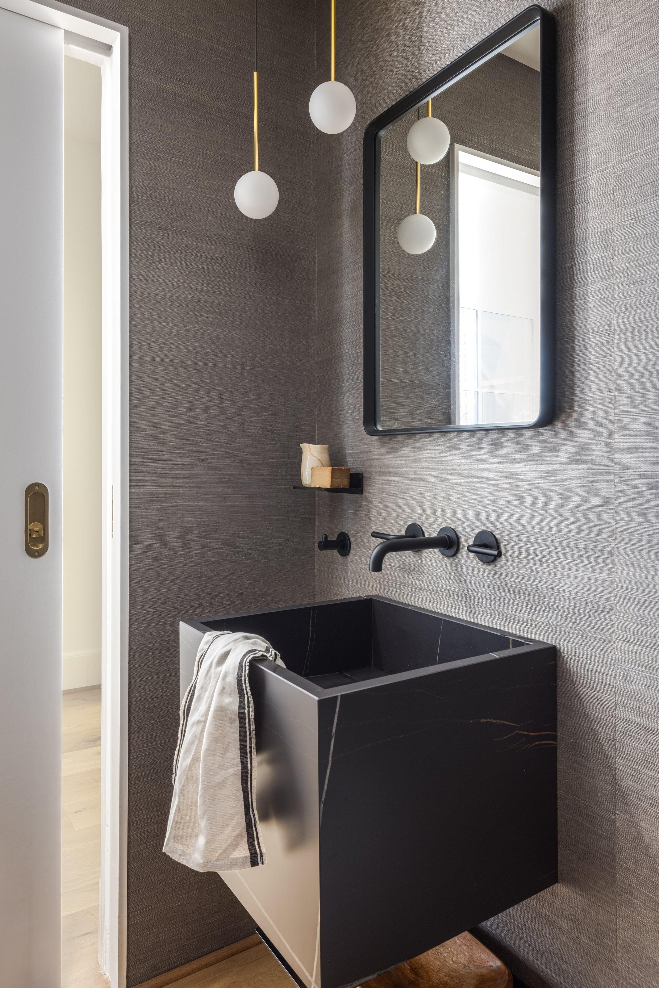 Powder room with a floating black stone basin, brass taps, a globe pendant and grey textured walls