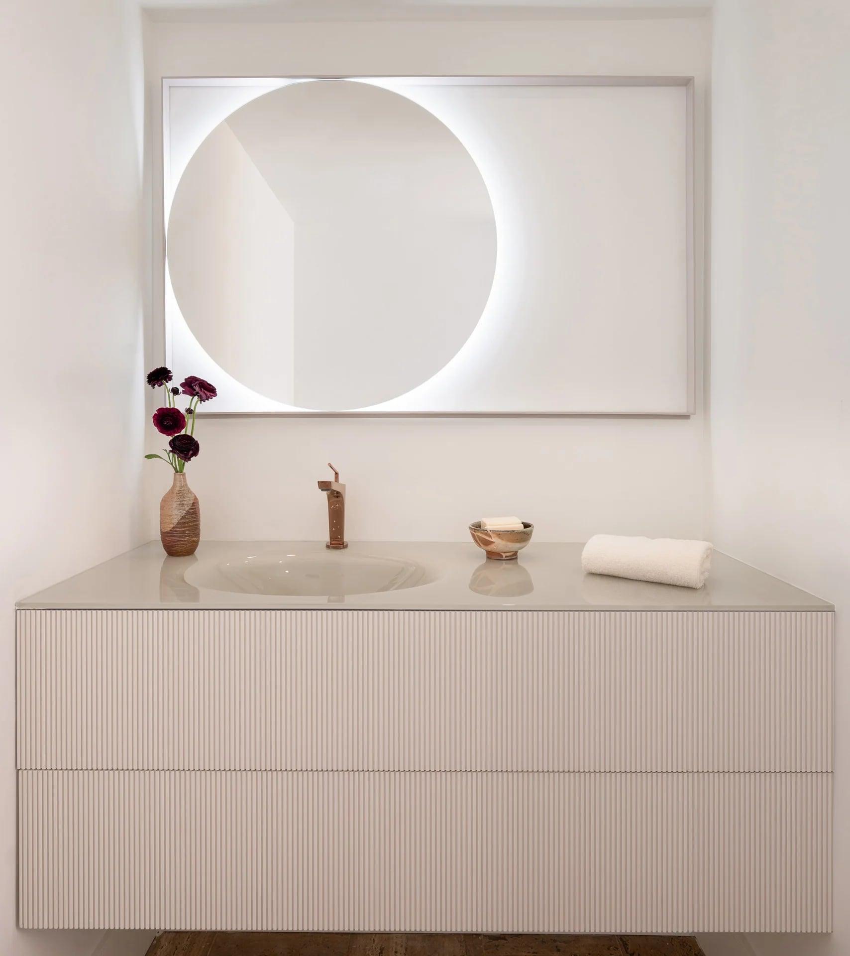 Reeded vanity with an integrated basin and a round backlit mirror