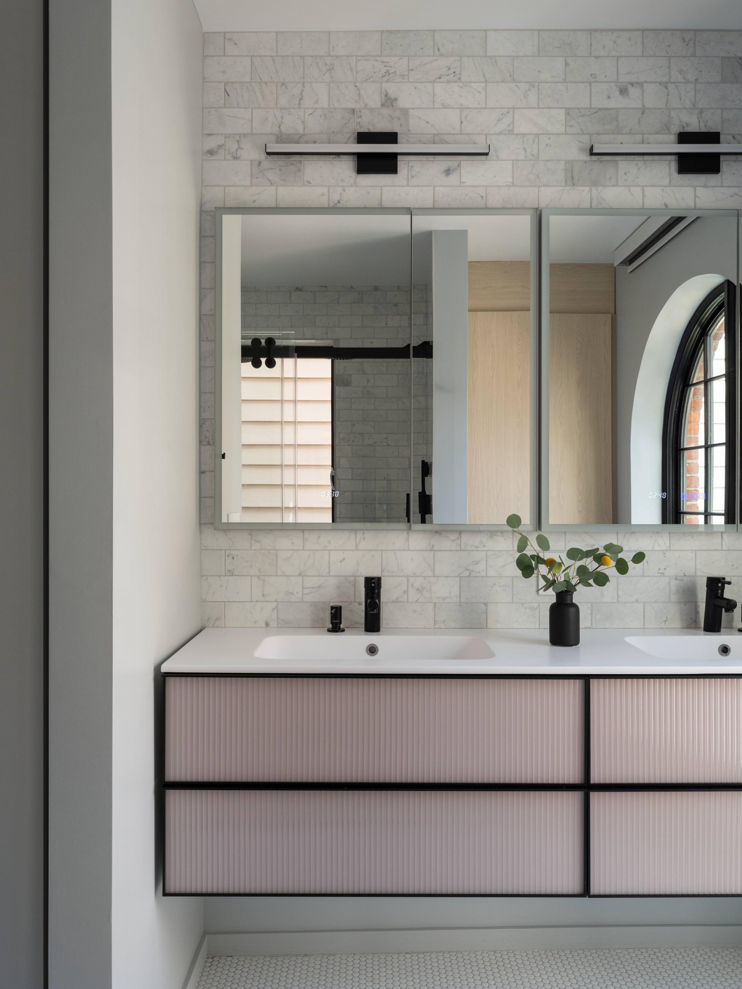 Double vanity with reeded pink drawers and a black frame under a wide mirror, on a white brick-tiled wall