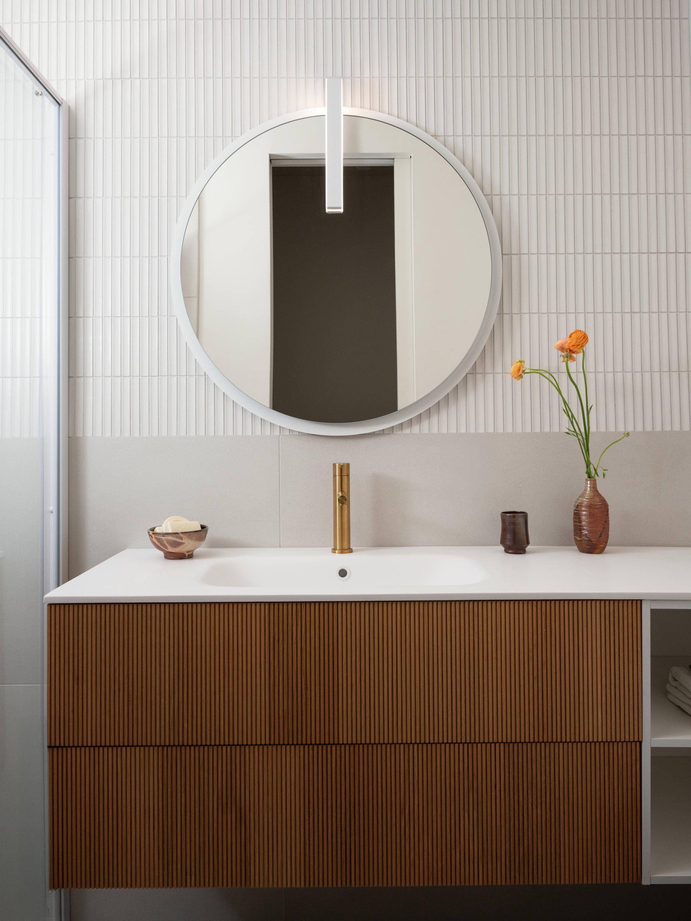 Walnut wall-hung vanity with a white basin under a round backlit mirror on white tile