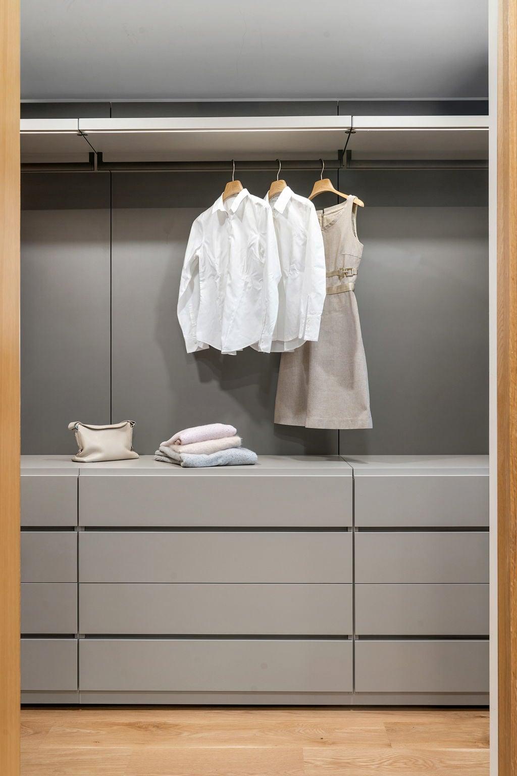 Open wardrobe in grey lacquer with hanging shirts over a chest of drawers, framed in oak