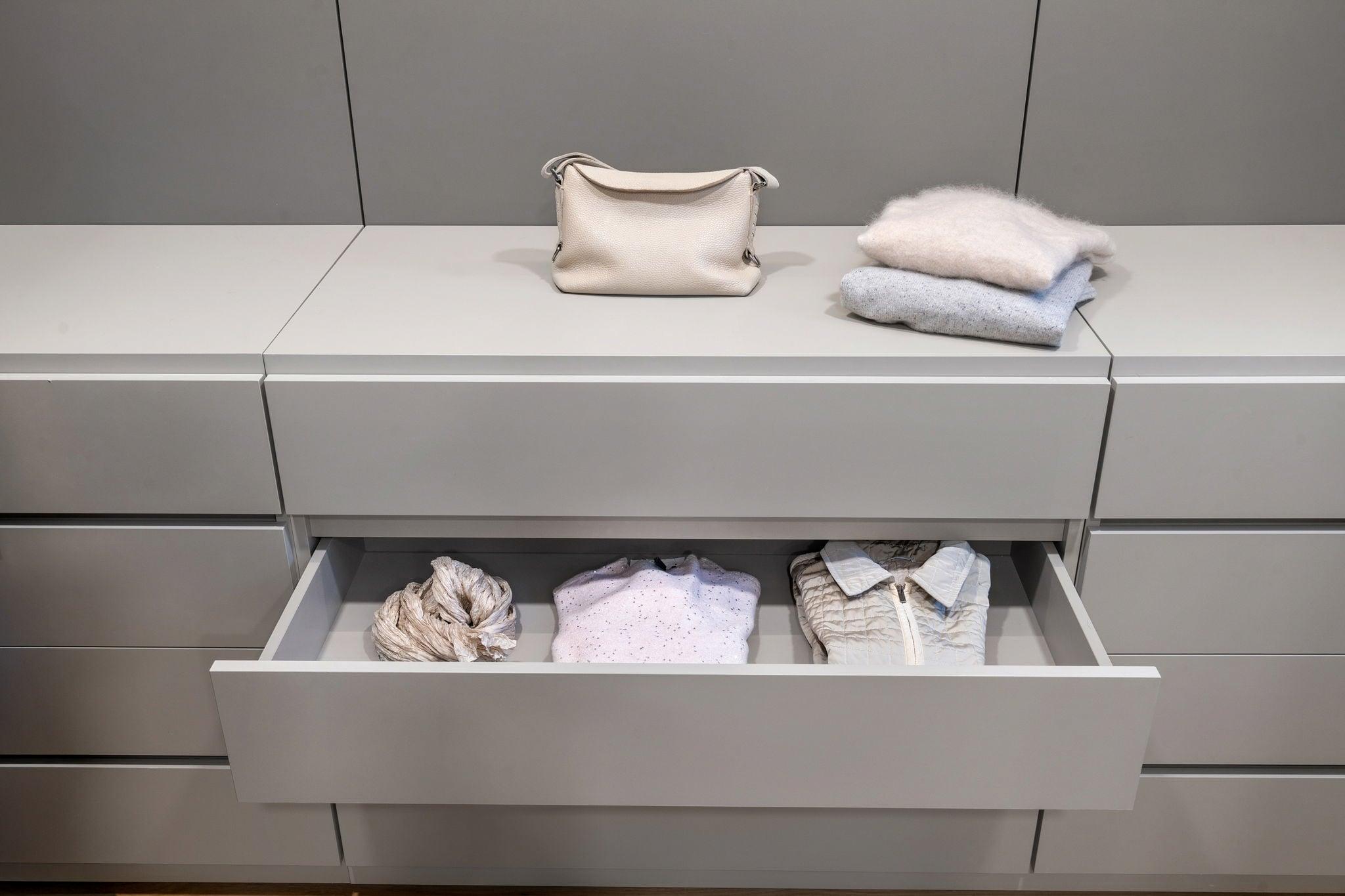 Grey lacquered drawer pulled out with folded shirts, a bag and towels on top