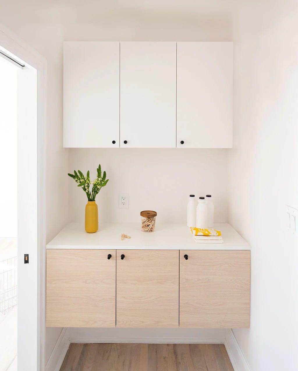White bar cabinets with a dark stone top, a shelf with flowers and a print