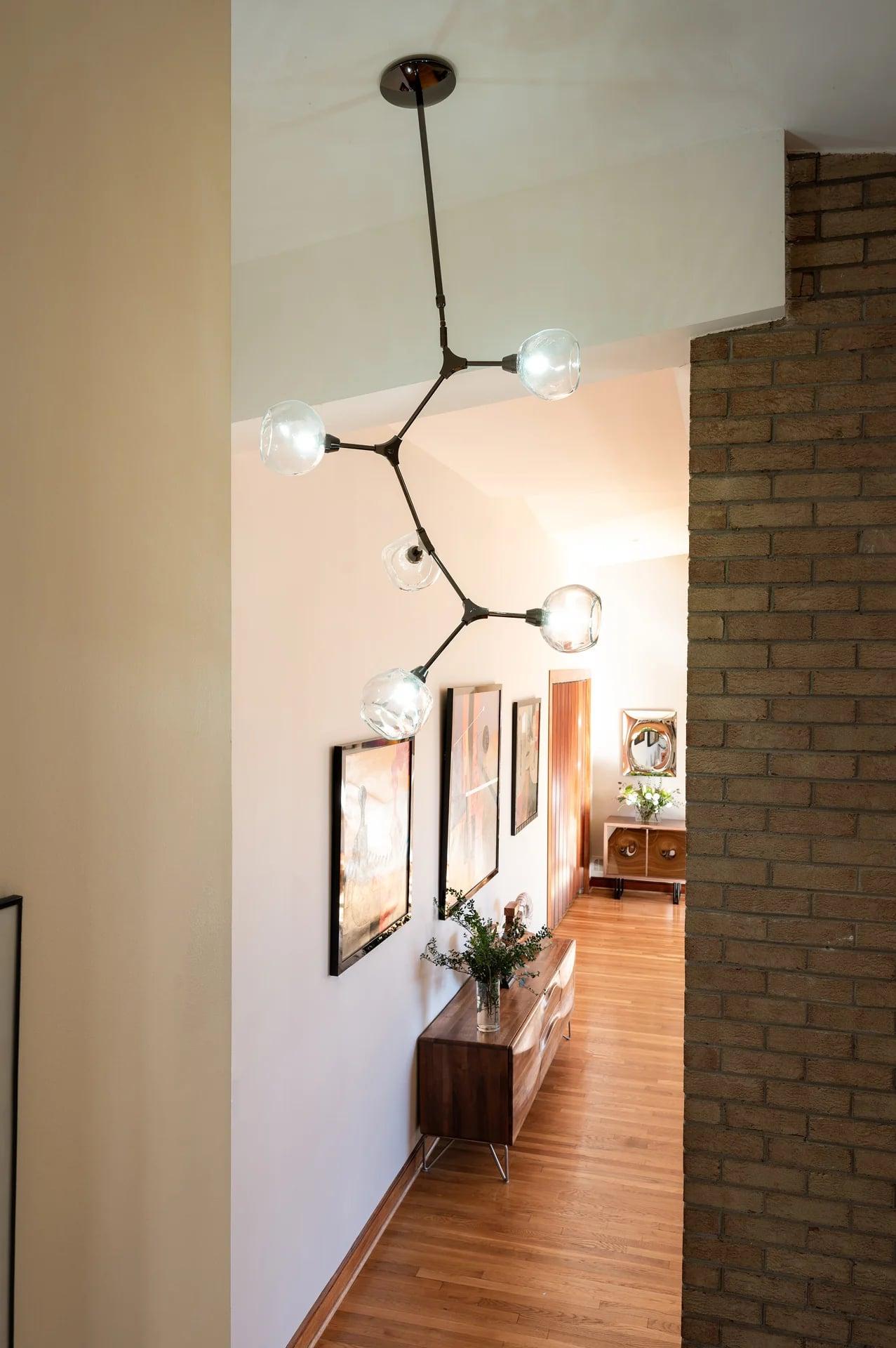 Double-height hallway with a brick wall and a glass chandelier