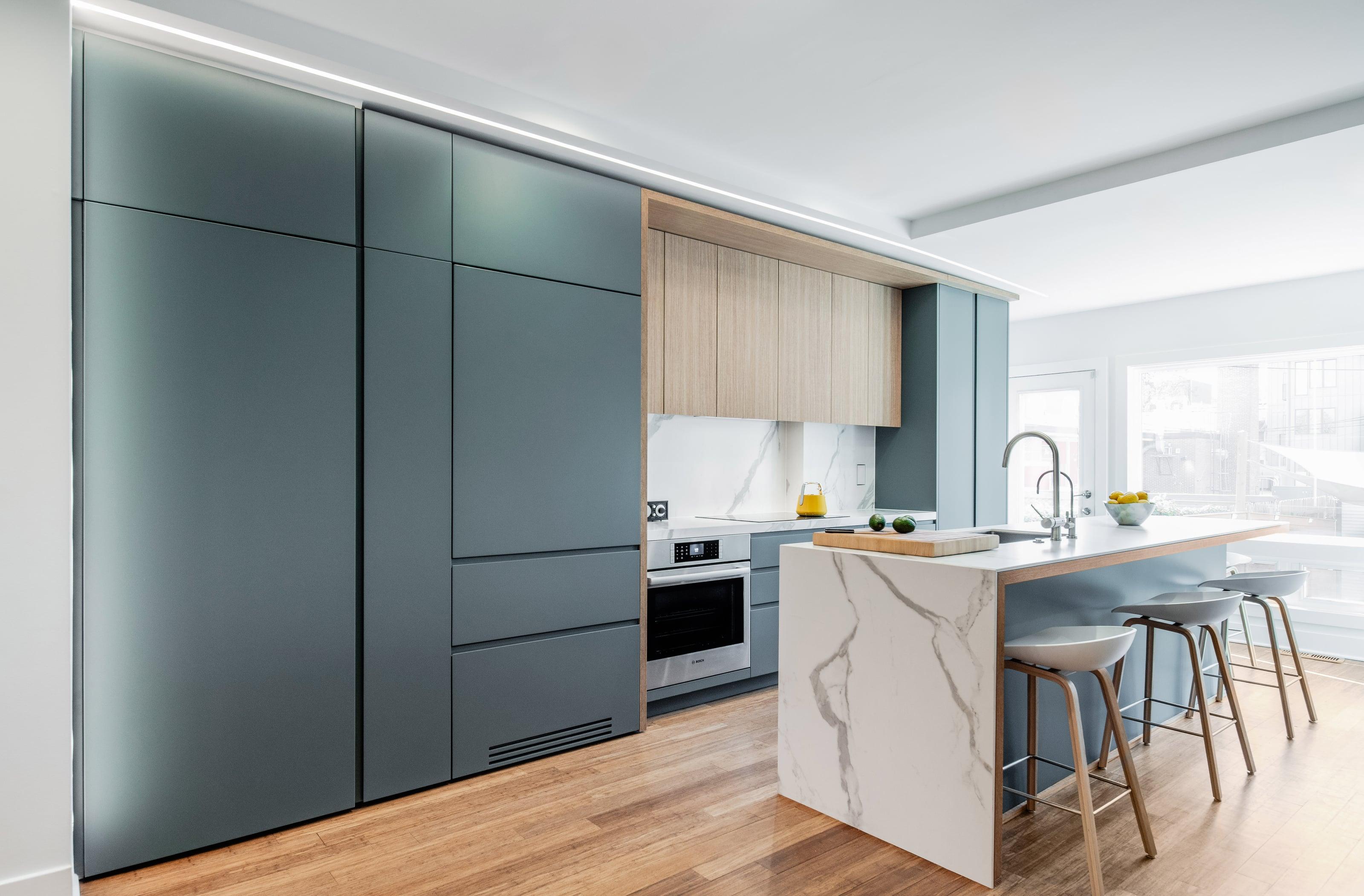 Kitchen with teal full-height cabinets, oak wall units and a white marble waterfall island with stools