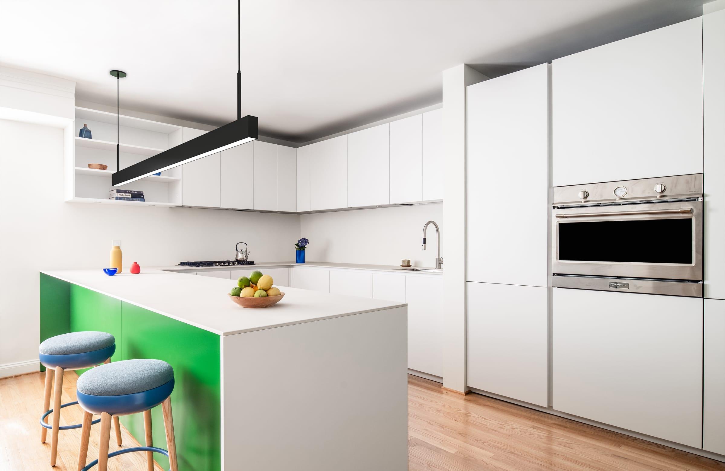 White kitchen with a green island, blue stools and a black pendant