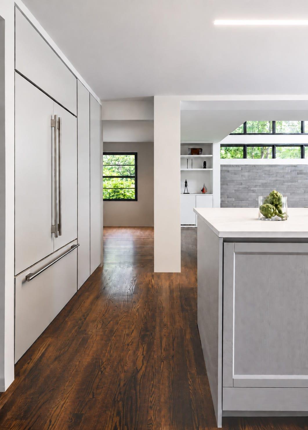 Grey tall units with steel handles along a corridor, the island and a window beyond