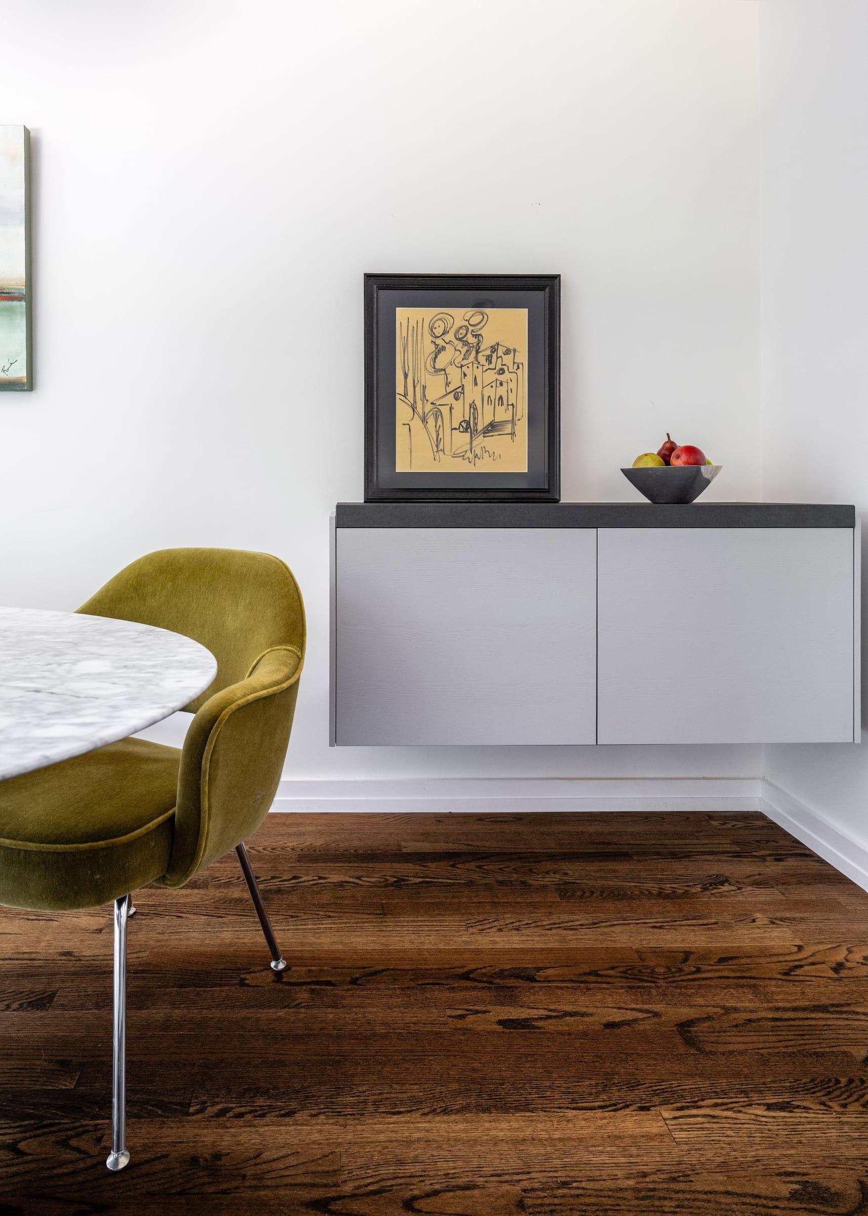 Grey floating sideboard under a framed drawing, an olive velvet chair at a marble table