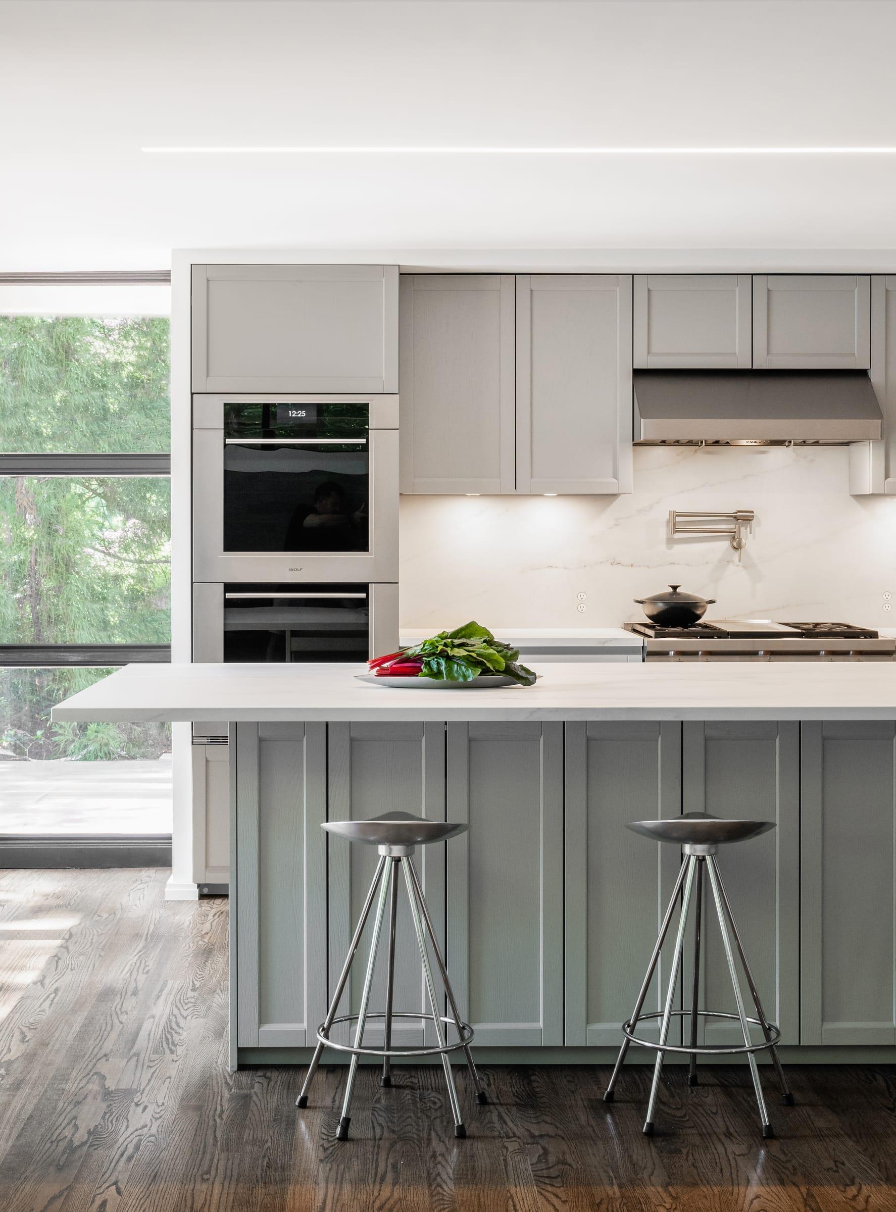 Grey shaker island with steel stools before grey tall units and a marble splashback