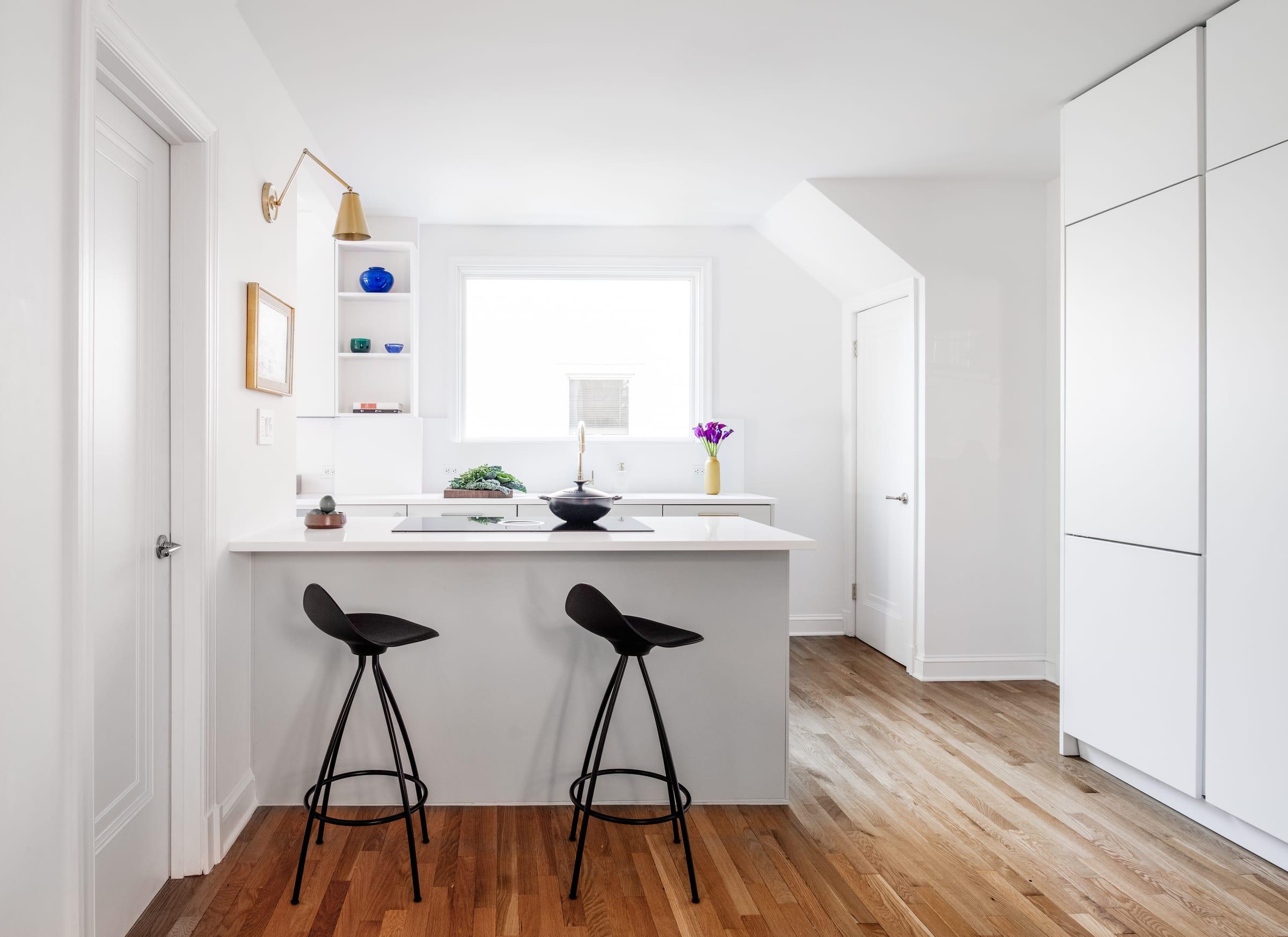 White peninsula with black stools in a bright kitchen