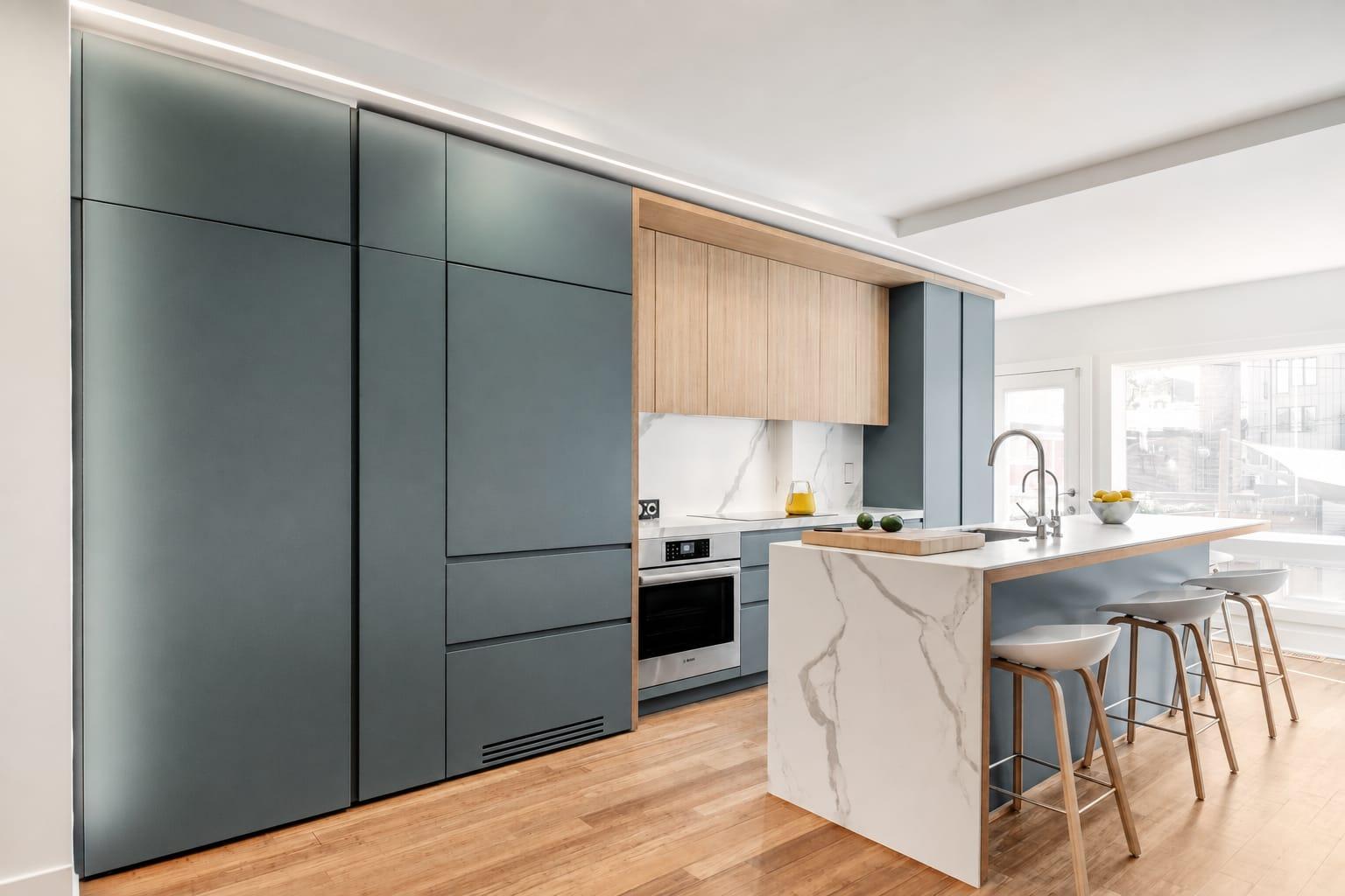 Kitchen with grey-green tall units, a marble island and stools by the window