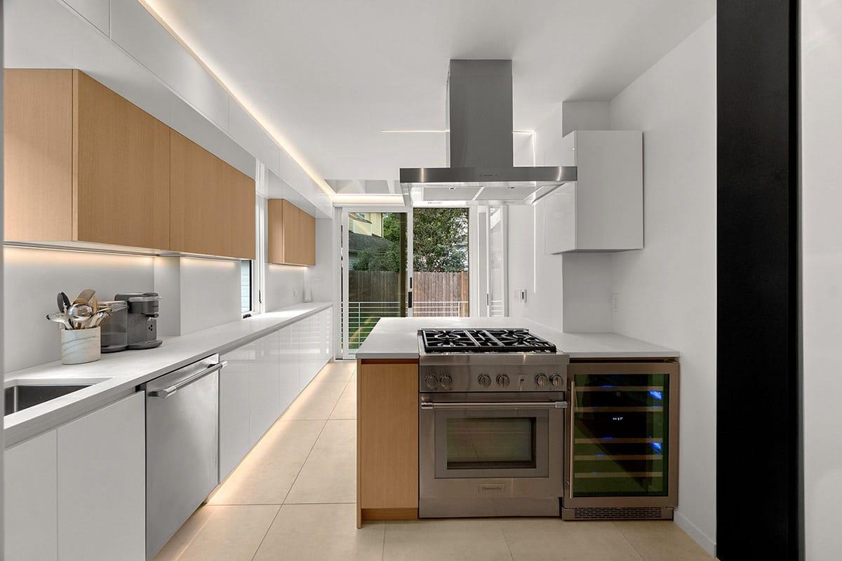 Galley kitchen in white and oak with a range and a steel hood, a garden door at the end