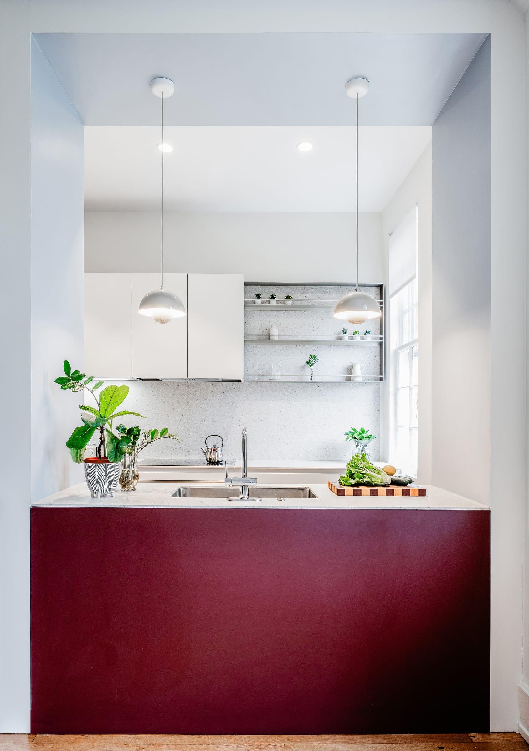 Burgundy island under glass pendants in a white kitchen