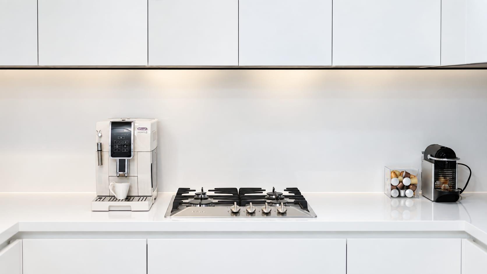 White kitchen with a gas hob and a coffee machine under white wall cabinets
