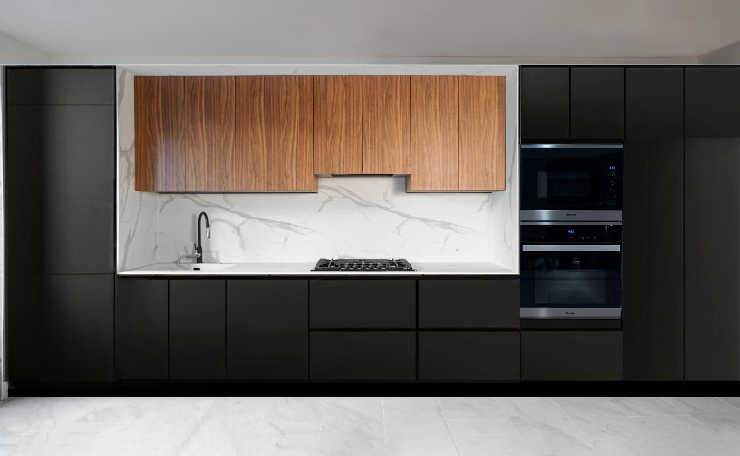 Black kitchen wall with walnut wall units over a marble splashback and built-in ovens