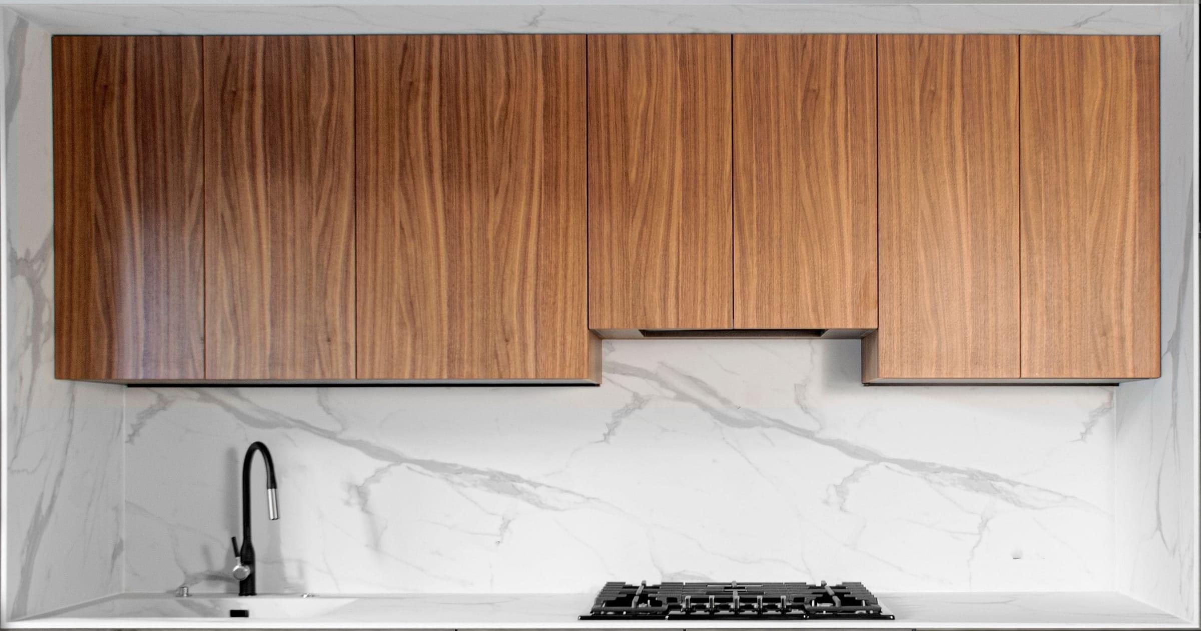 Walnut wall units stepping down over a marble splashback, the tap and the hob below