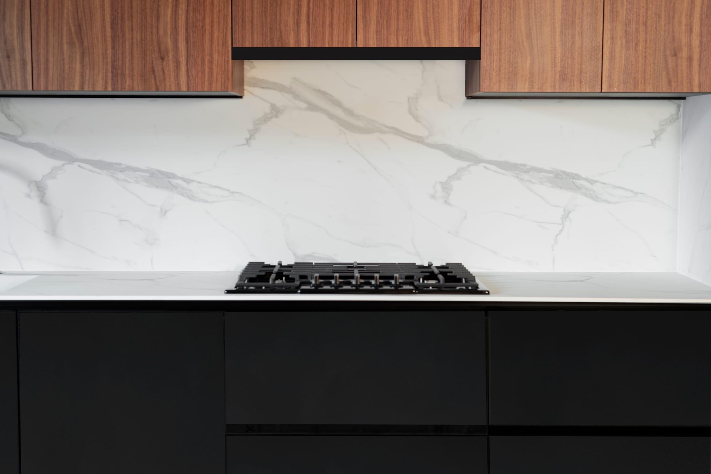 Walnut wall units over a marble splashback and a gas hob on black drawers