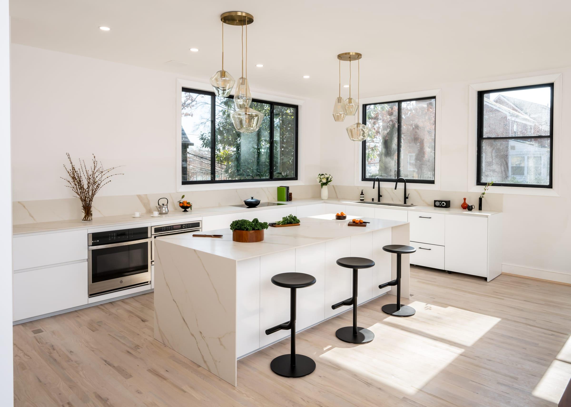 White kitchen with a marble island and black stools under brass pendants