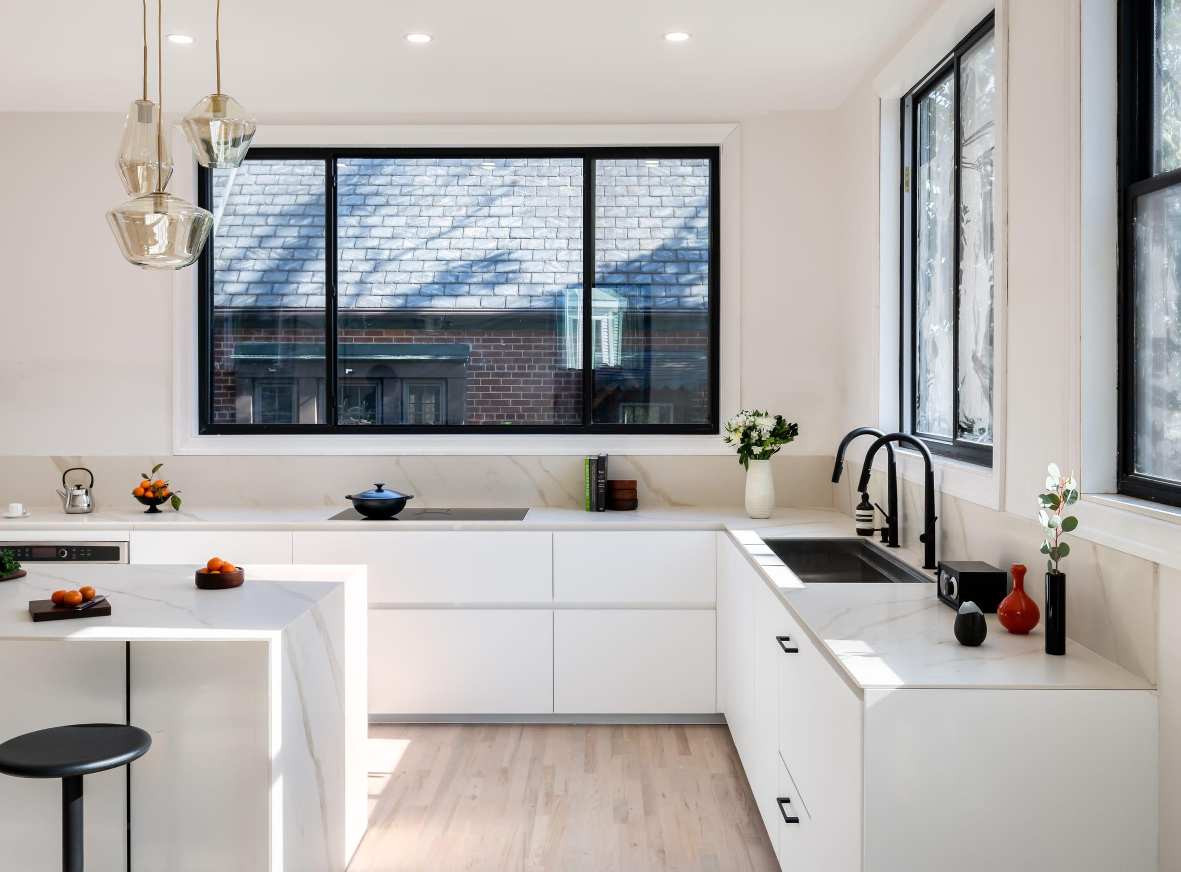 White kitchen with a marble peninsula under a wide window