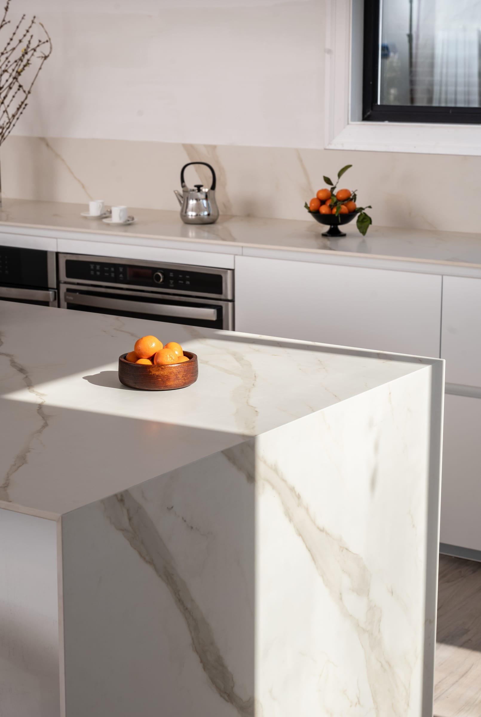 Marble worktop corner with a bowl of oranges in front of built-in ovens