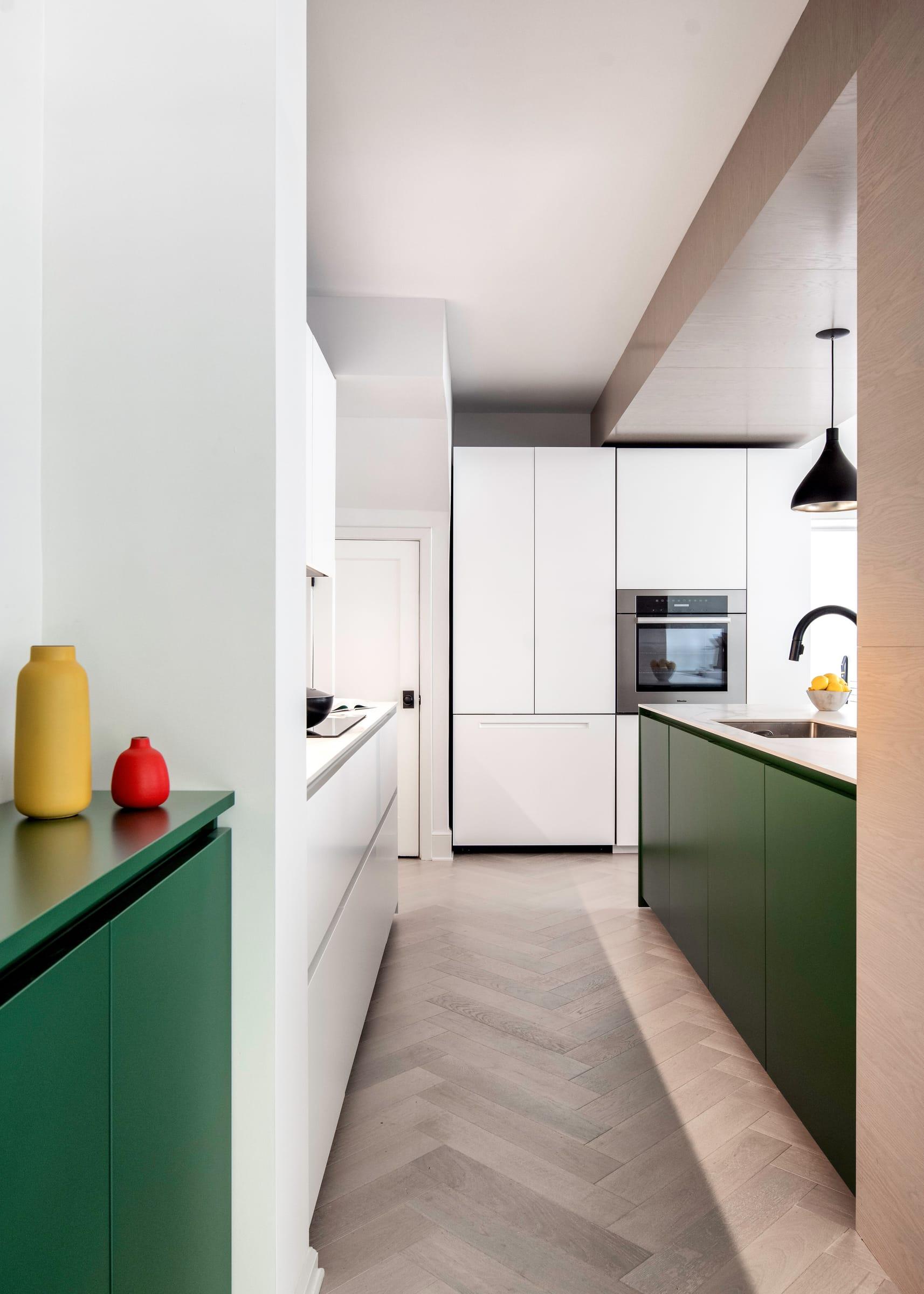 White kitchen beyond a green cabinet and a herringbone floor