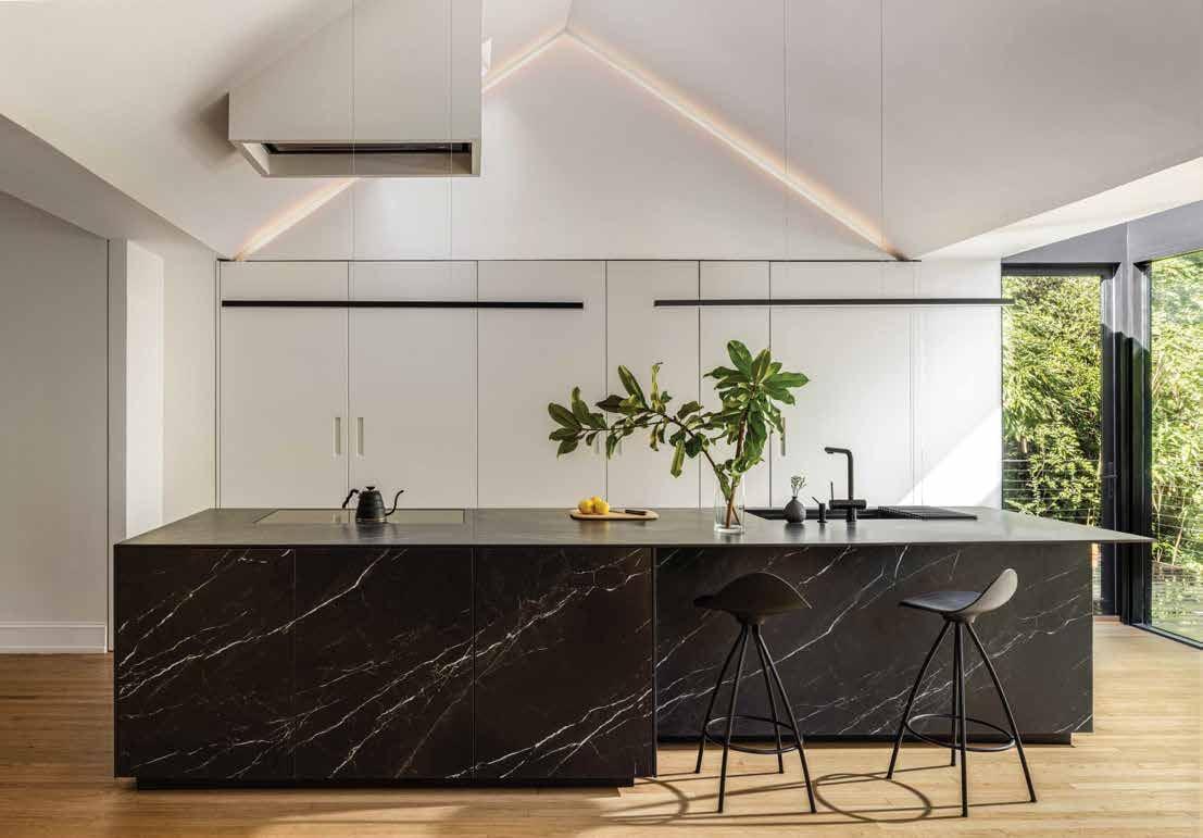 Black marble island with bar stools under a vaulted ceiling, white tall units behind