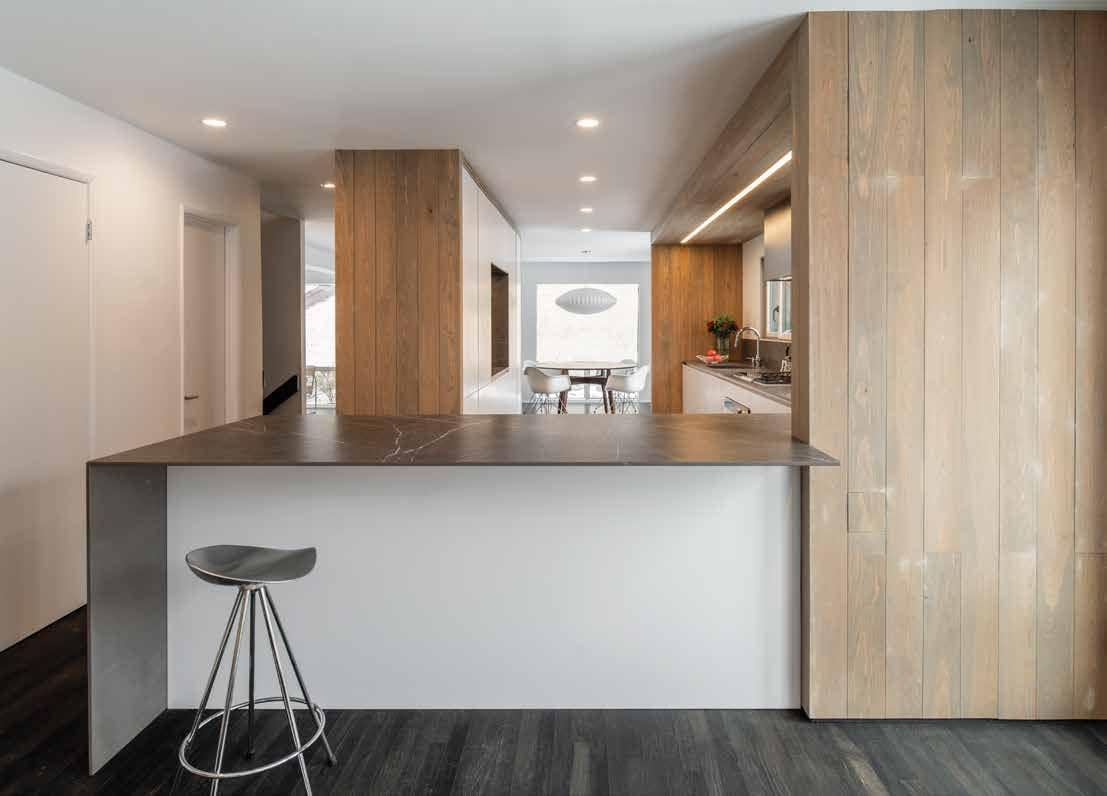 Kitchen peninsula with a stool, a tall wood-clad unit beside it and a corridor beyond